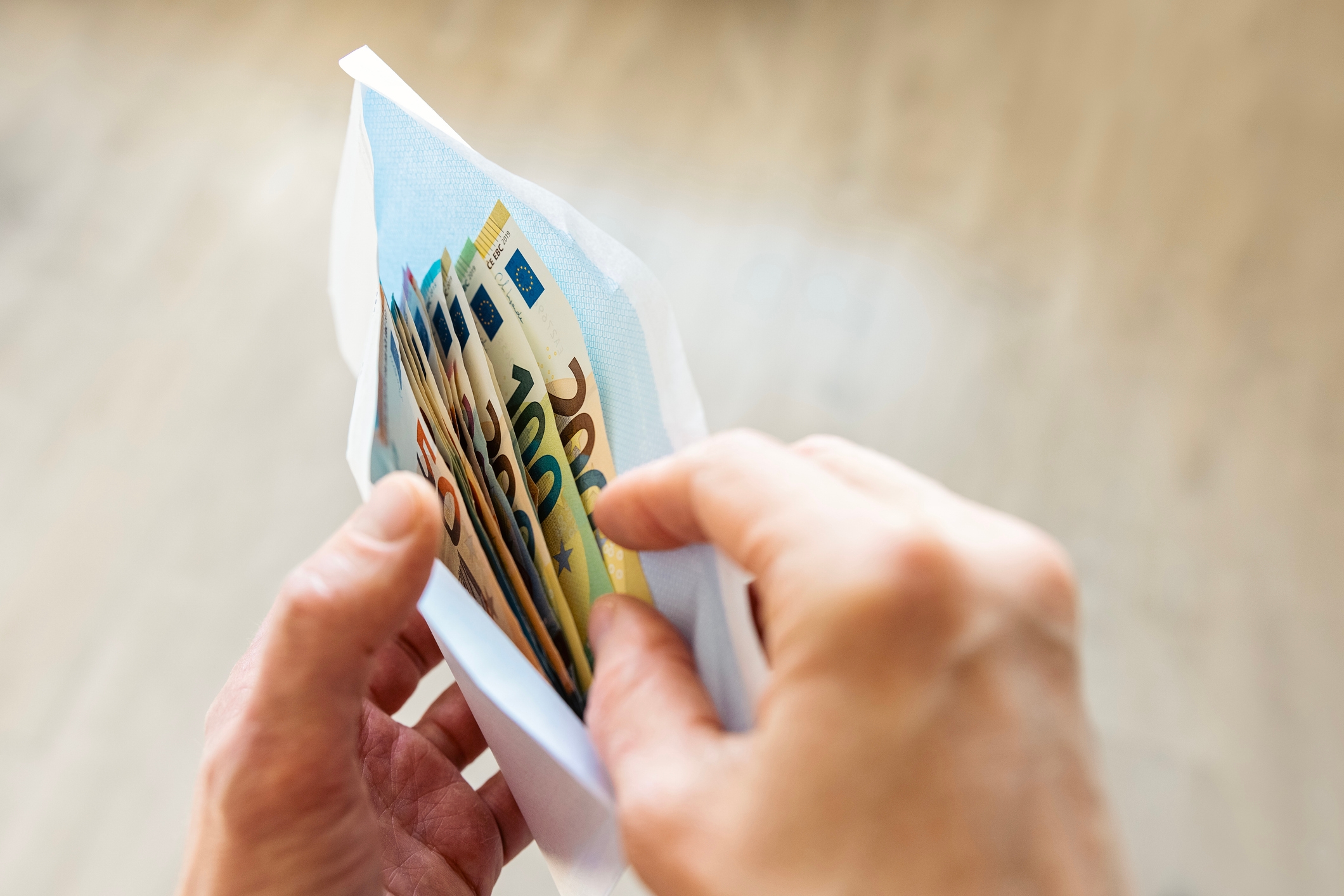 Hands holding an envelope filled with Euro banknotes, suggesting a financial transaction or payment