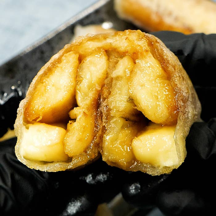 バナナとキャラメルを包んだデザートが、黒い手袋をした手に持たれている。