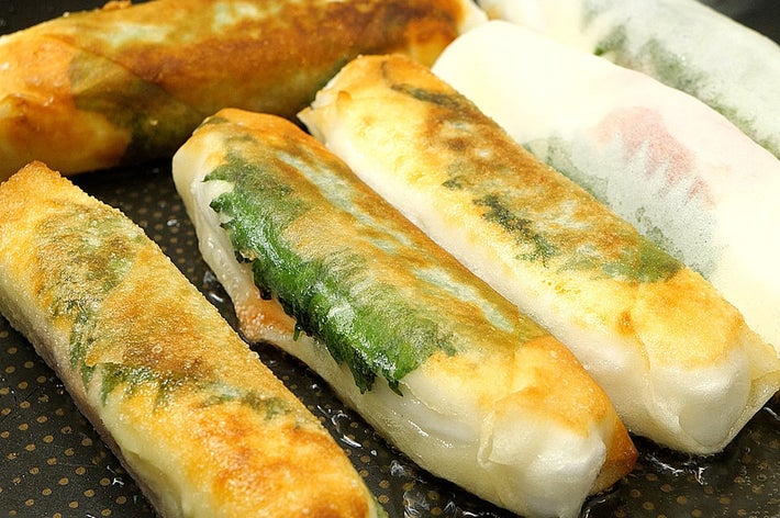 焼かれている複数の春巻きがフライパンで調理中。サクサクした表面と具材が透けて見える。
