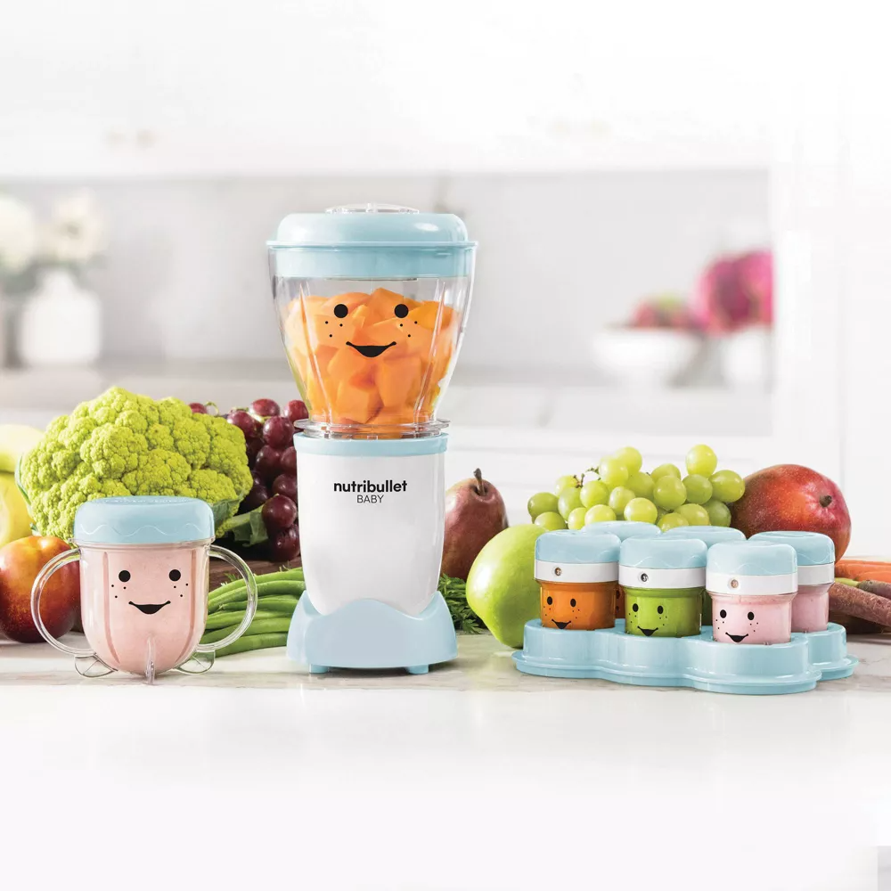 Nutribullet Baby Blender Set dengan desain wajah tersenyum, dikelilingi oleh buah -buahan dan sayuran di meja dapur