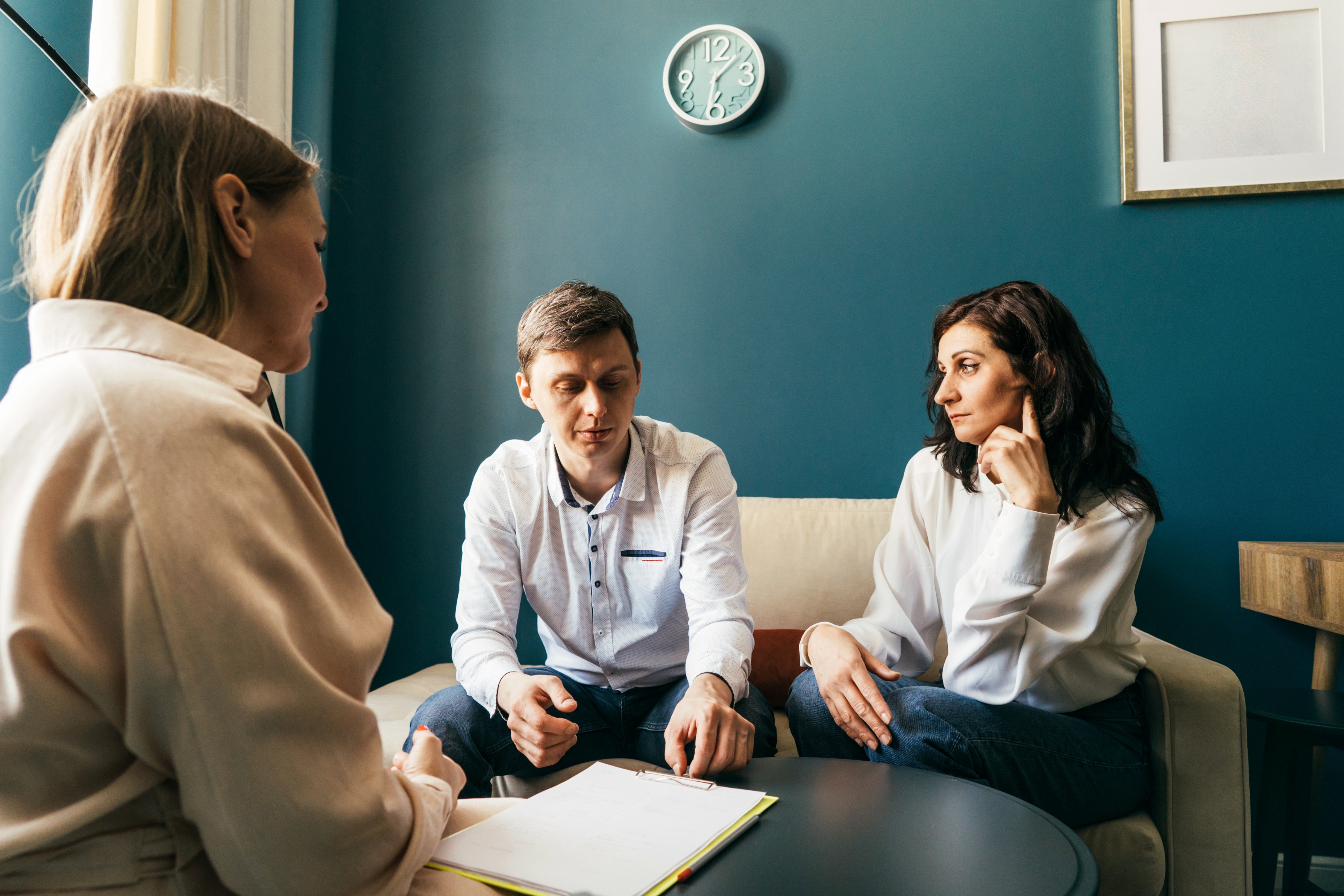 Three people are in a therapy session; a couple is seated across from a therapist, engaged in discussion