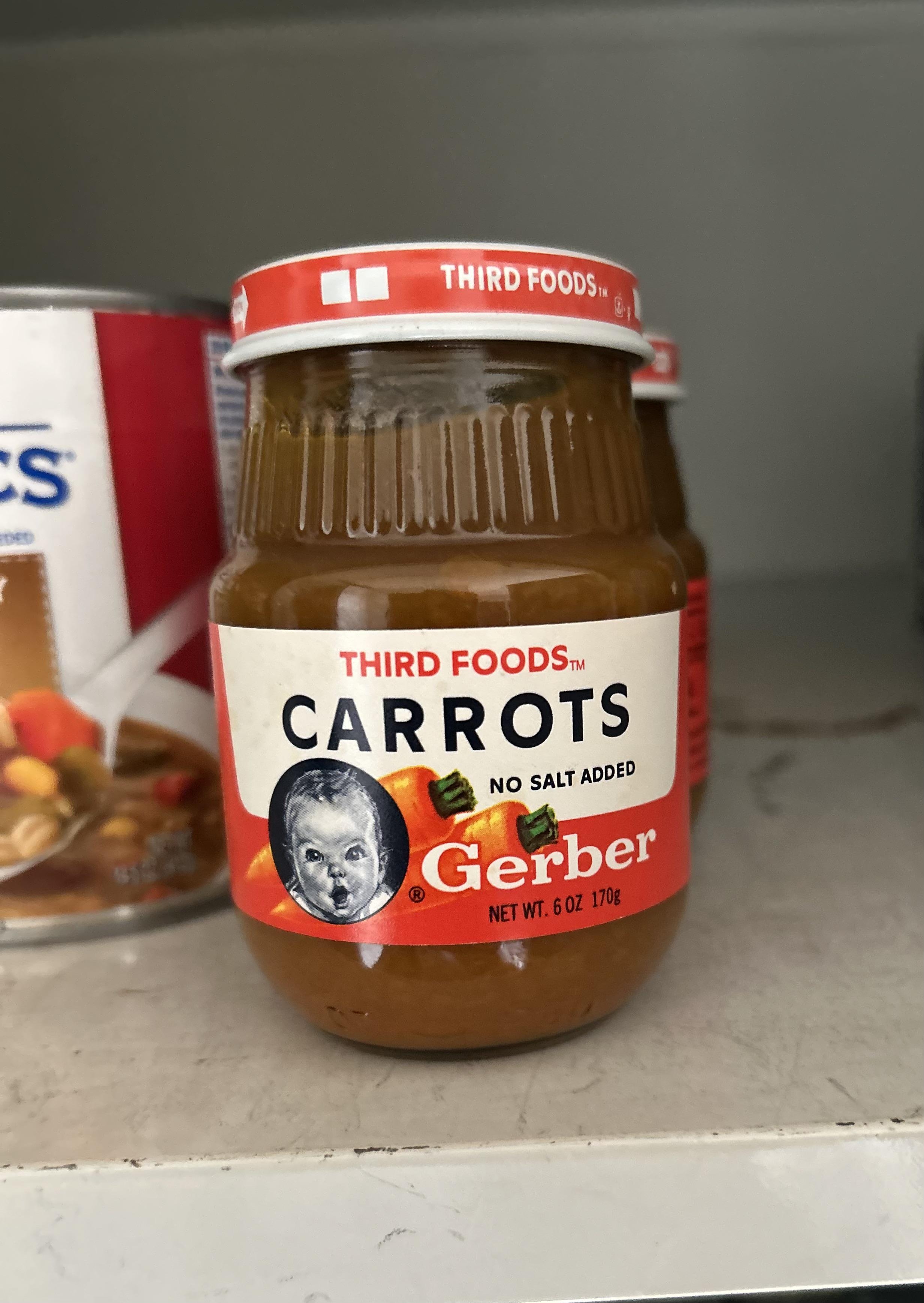 Jar of Gerber baby food labeled "Carrots, No Salt Added," with other jars partially visible in the background