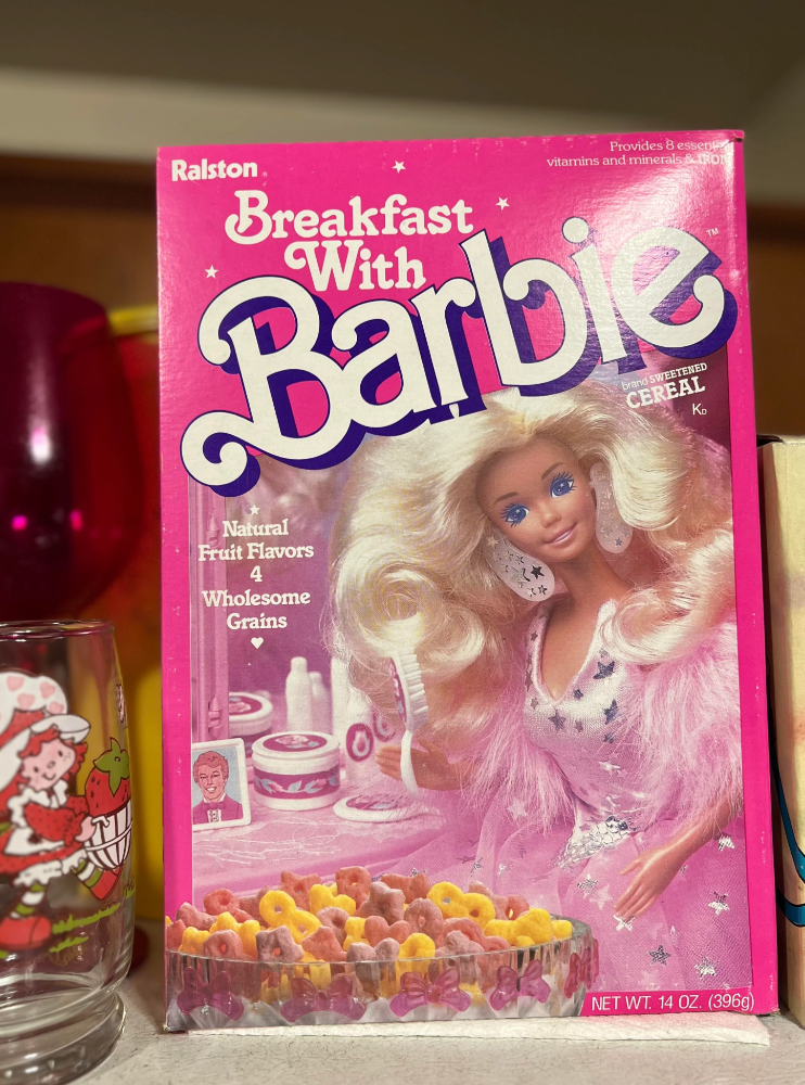 "Cereal box titled 'Breakfast with Barbie' featuring Barbie with wavy hair, wearing a pink feather outfit. Contains cereals with natural fruit flavors."