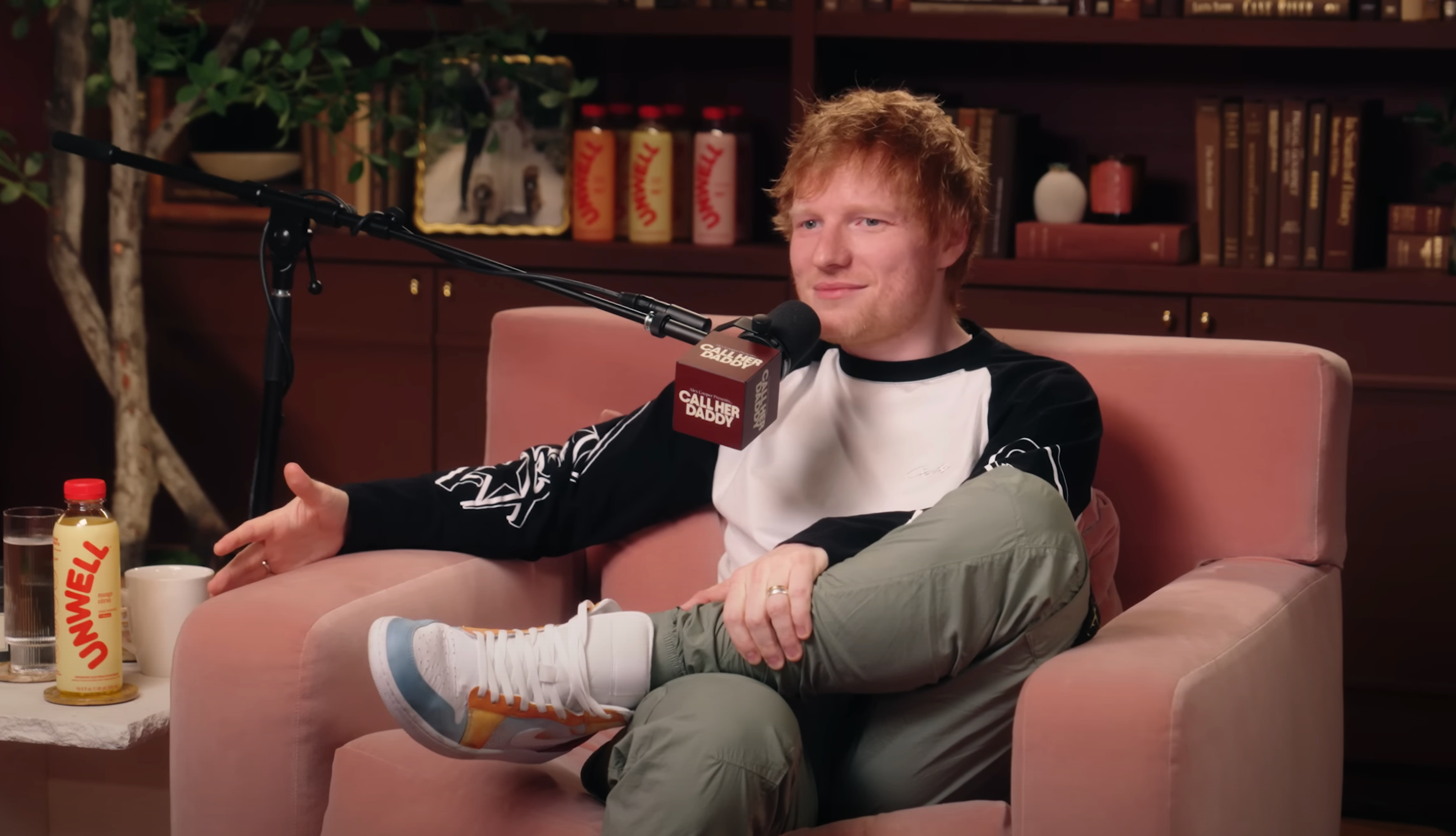 Singer with casual black and white top and patterned sneakers sits on a pink chair during a podcast interview
