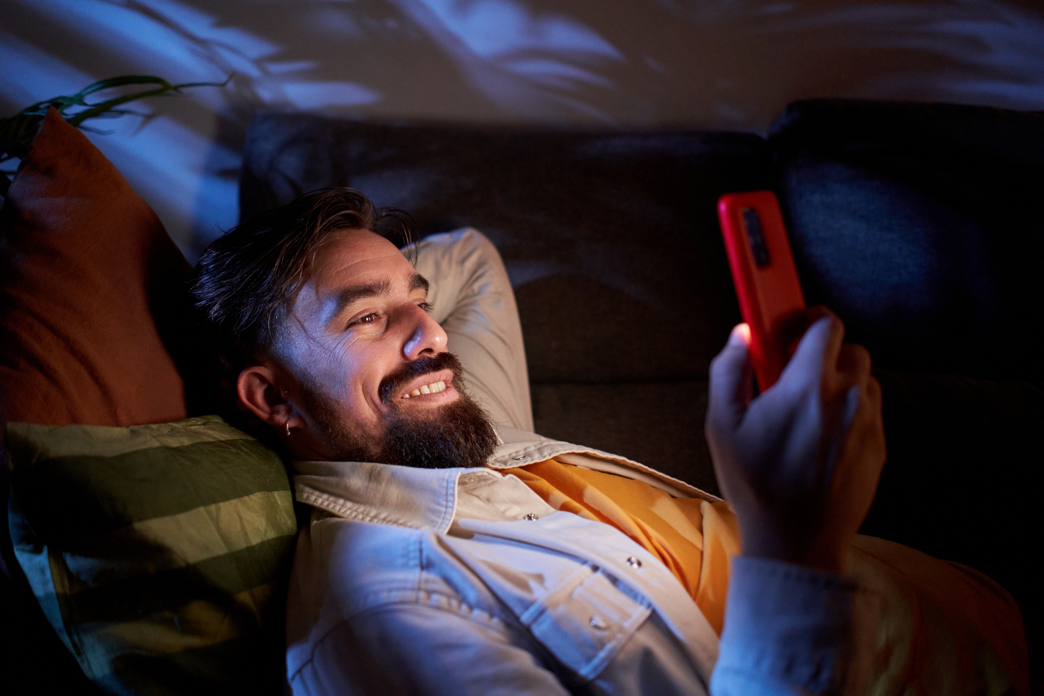 Personen slapper av på en sofa, smiler mens han ser på smarttelefonen, muligens ser på noe morsomt eller leser en positiv melding