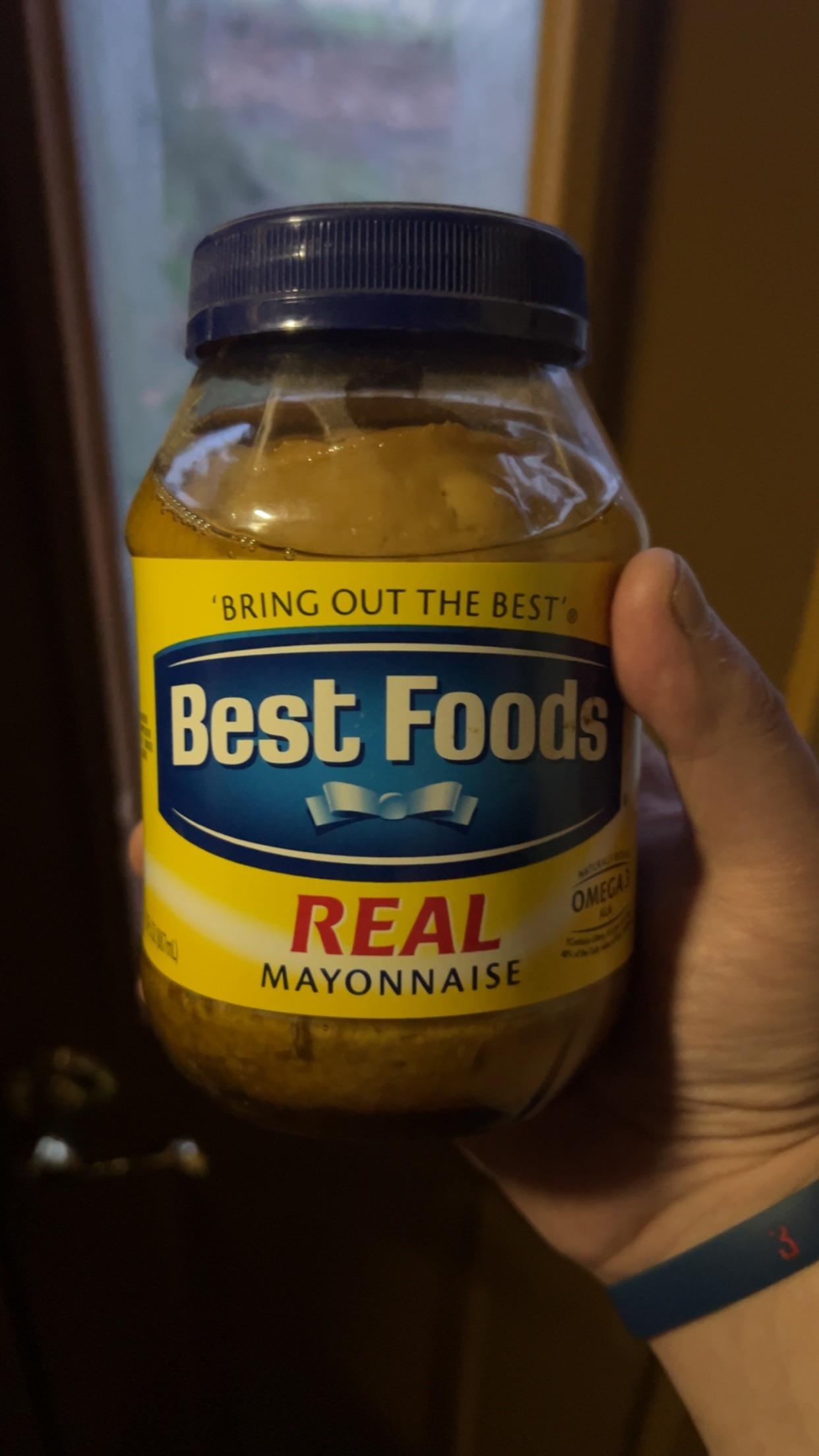 A hand holding a jar of Best Foods real mayonnaise
