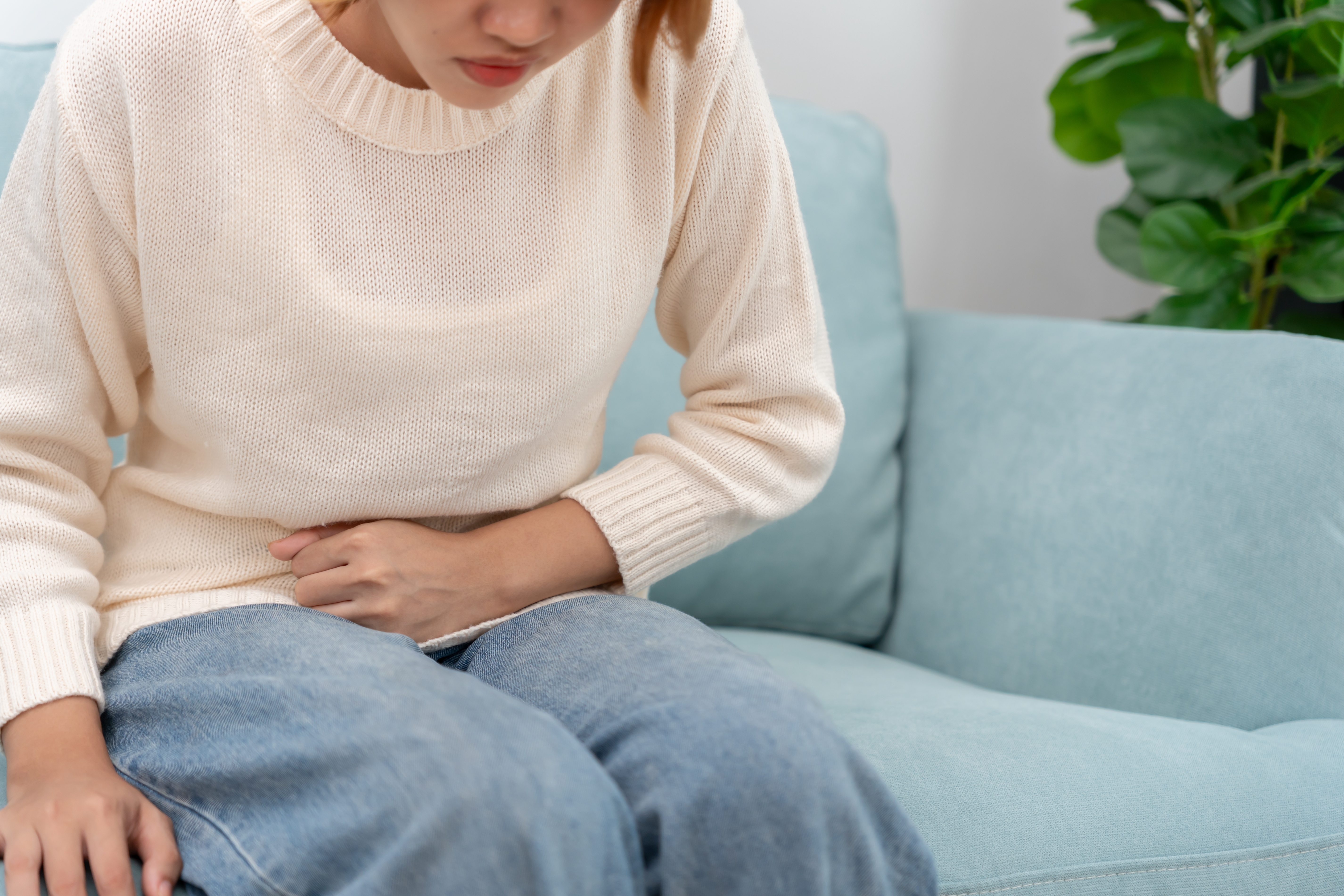 Person som sitter på en sofa, ser ut til å oppleve ubehag i magen, holde magen med et smertefullt uttrykk