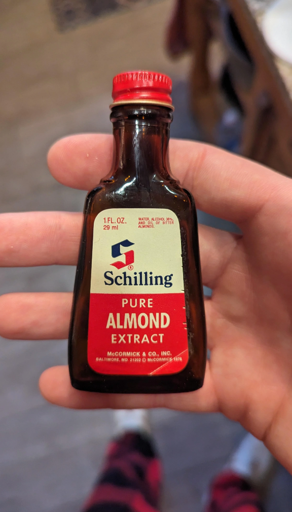 Person holding a small bottle of Schilling Pure Almond Extract, labeled with volume and manufacturer details
