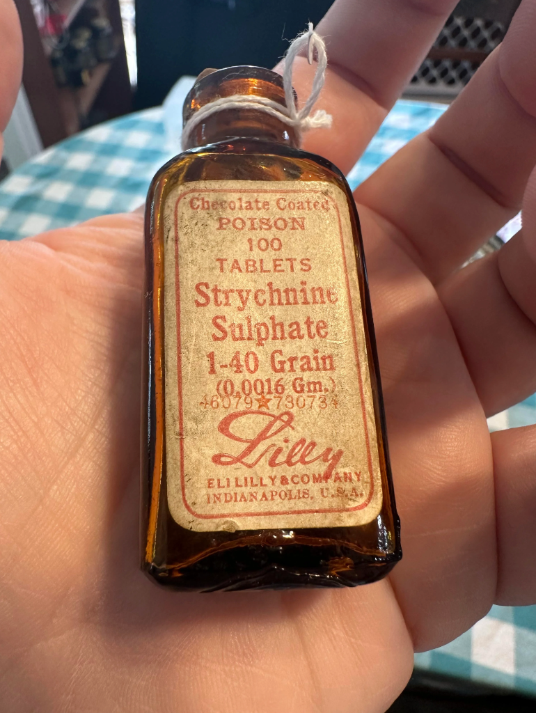Small brown glass bottle labeled "Chocolate Coated Poison" with "Strychnine Sulphate" and "Eli Lilly & Company, Indianapolis."