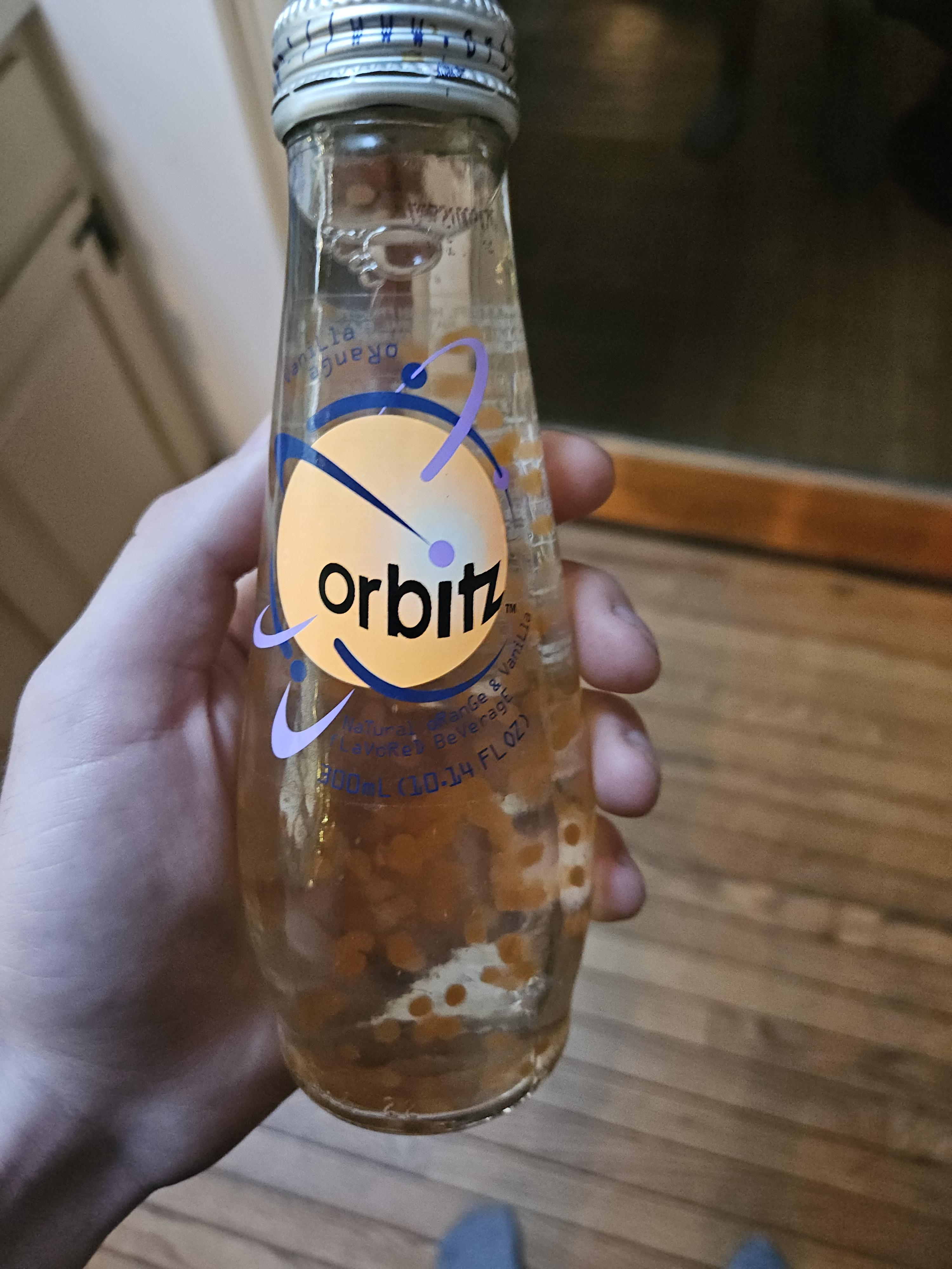 A hand holding a clear bottle of Orbitz, a beverage with small floating spheres inside