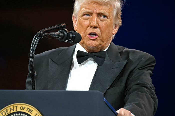 A person in a tuxedo speaks at a lectern with a seal
