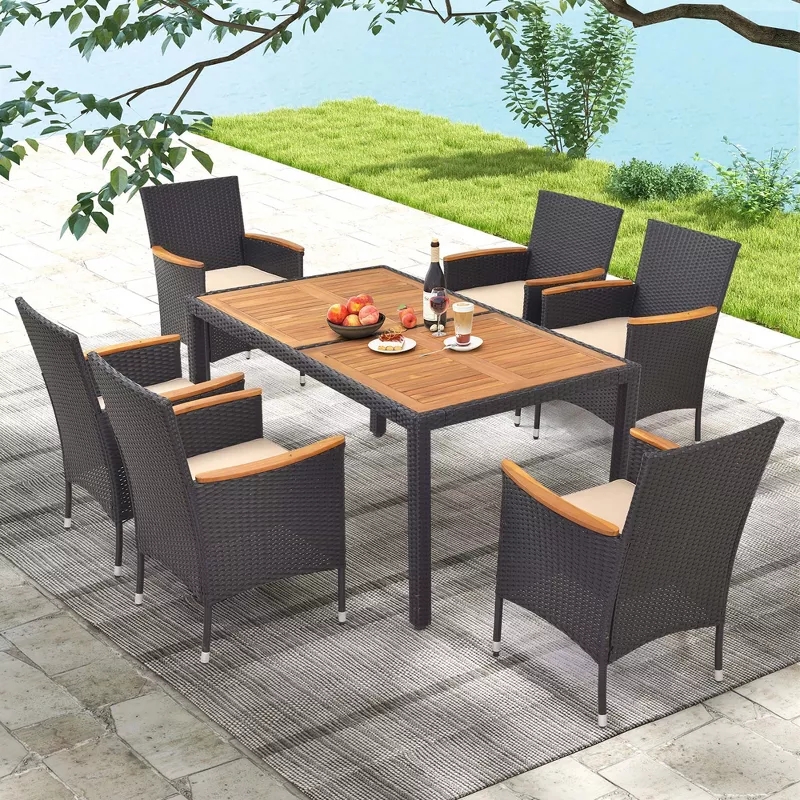 Outdoor patio set with six wicker chairs and a wooden table, arranged on a stone-tiled area. Items on the table include fruit and beverages
