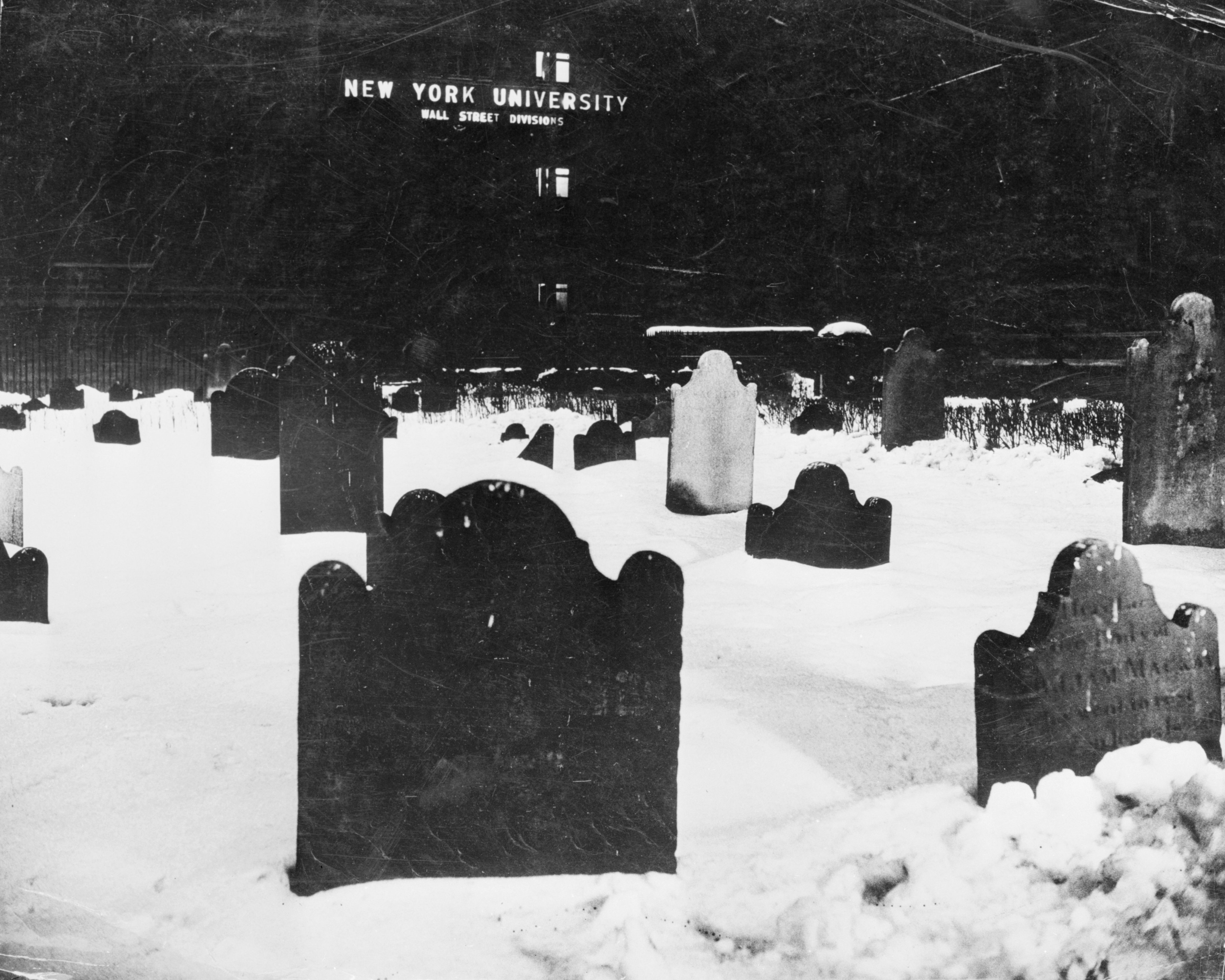 Gravestones in snow at night with a New York University building in the background