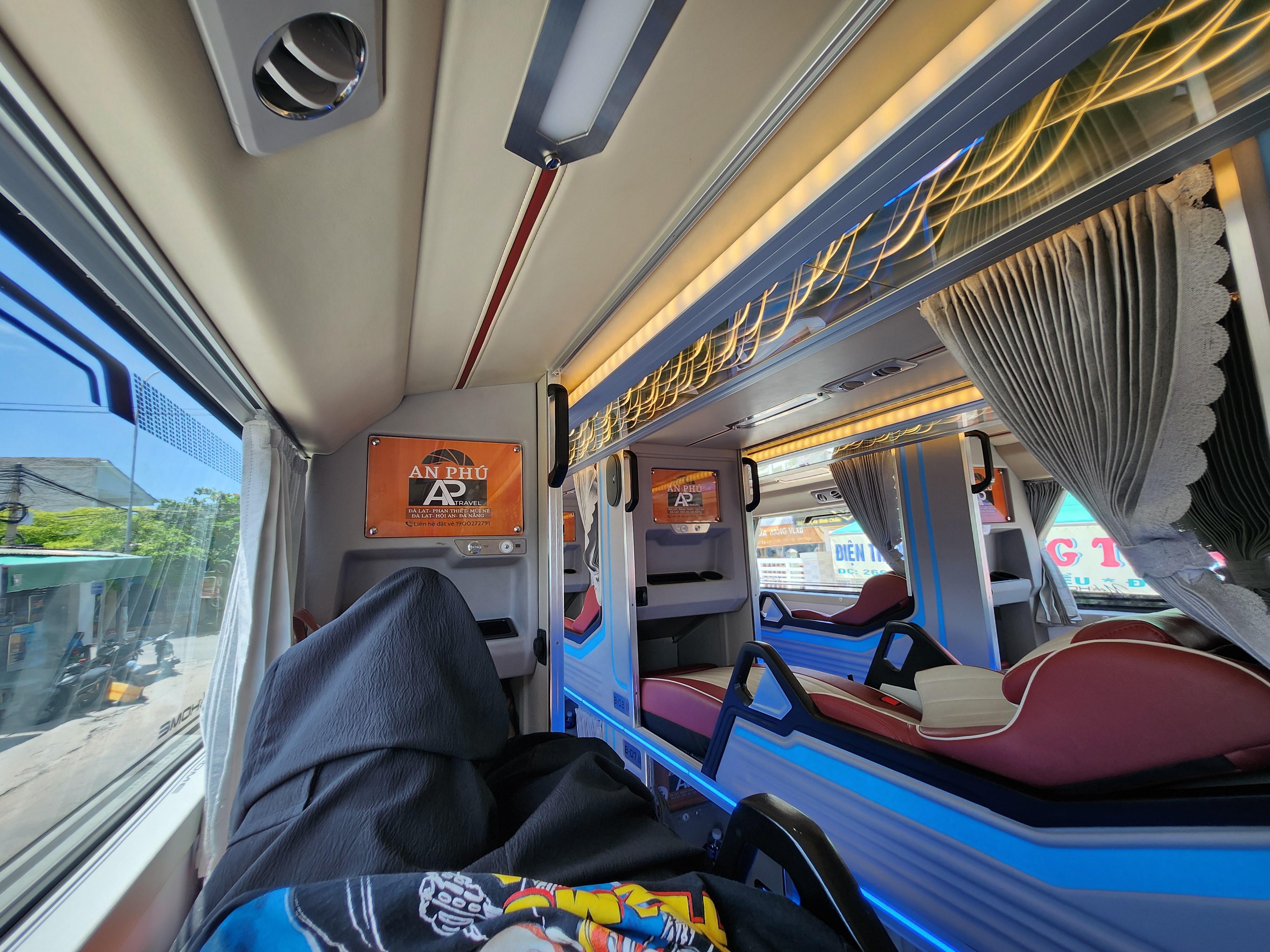 Bus interior with plush reclining seats, privacy curtains, and individual monitors showing an &quot;An Phú&quot; screen