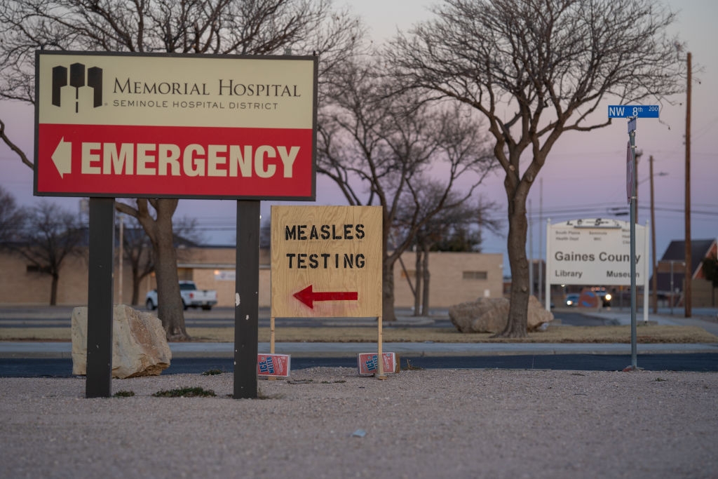 Signs outside a hospital point to emergency room and measles testing area, emphasizing public health response
