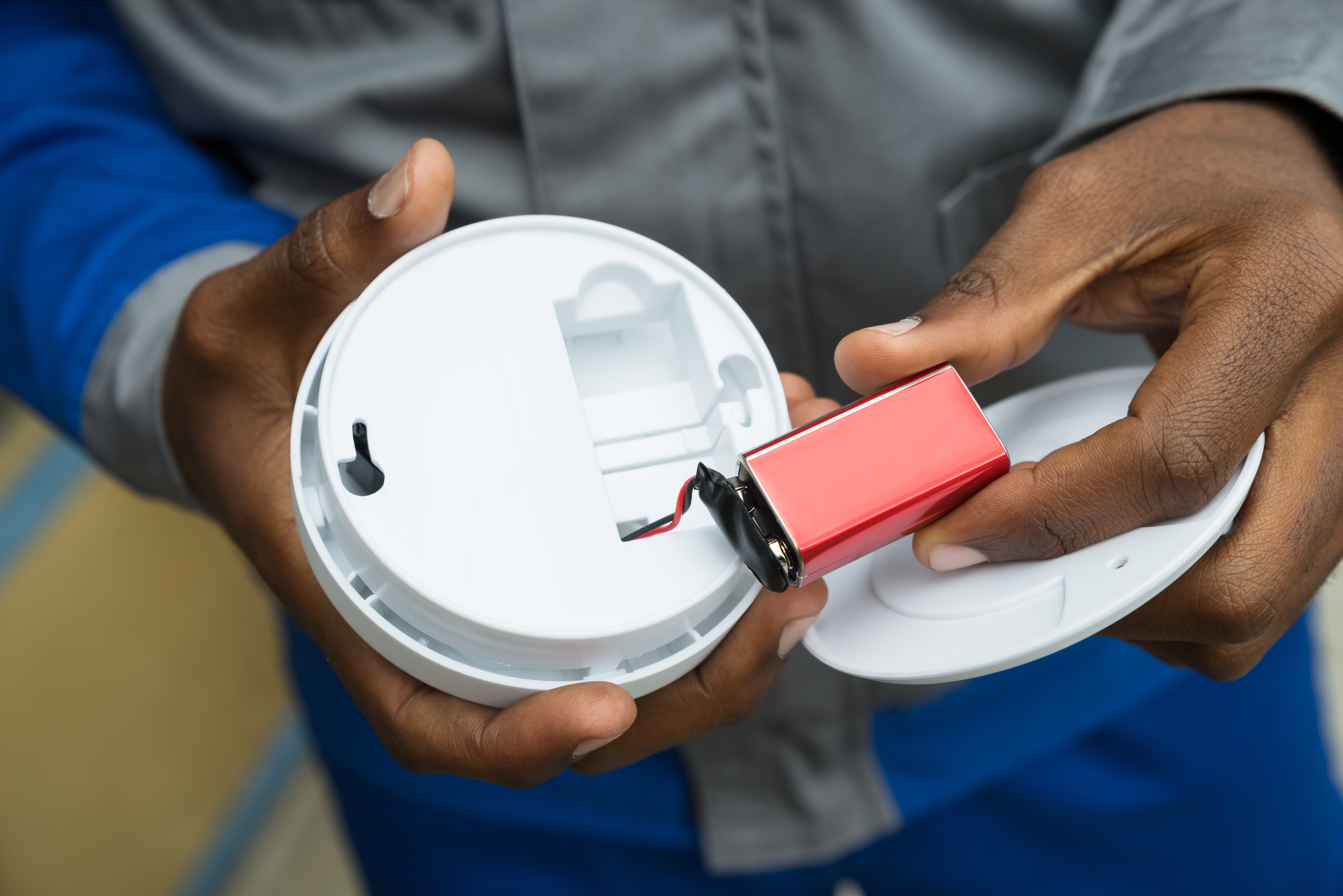 A person inserts a rectangular battery into a smoke detector, showcasing a home safety setup