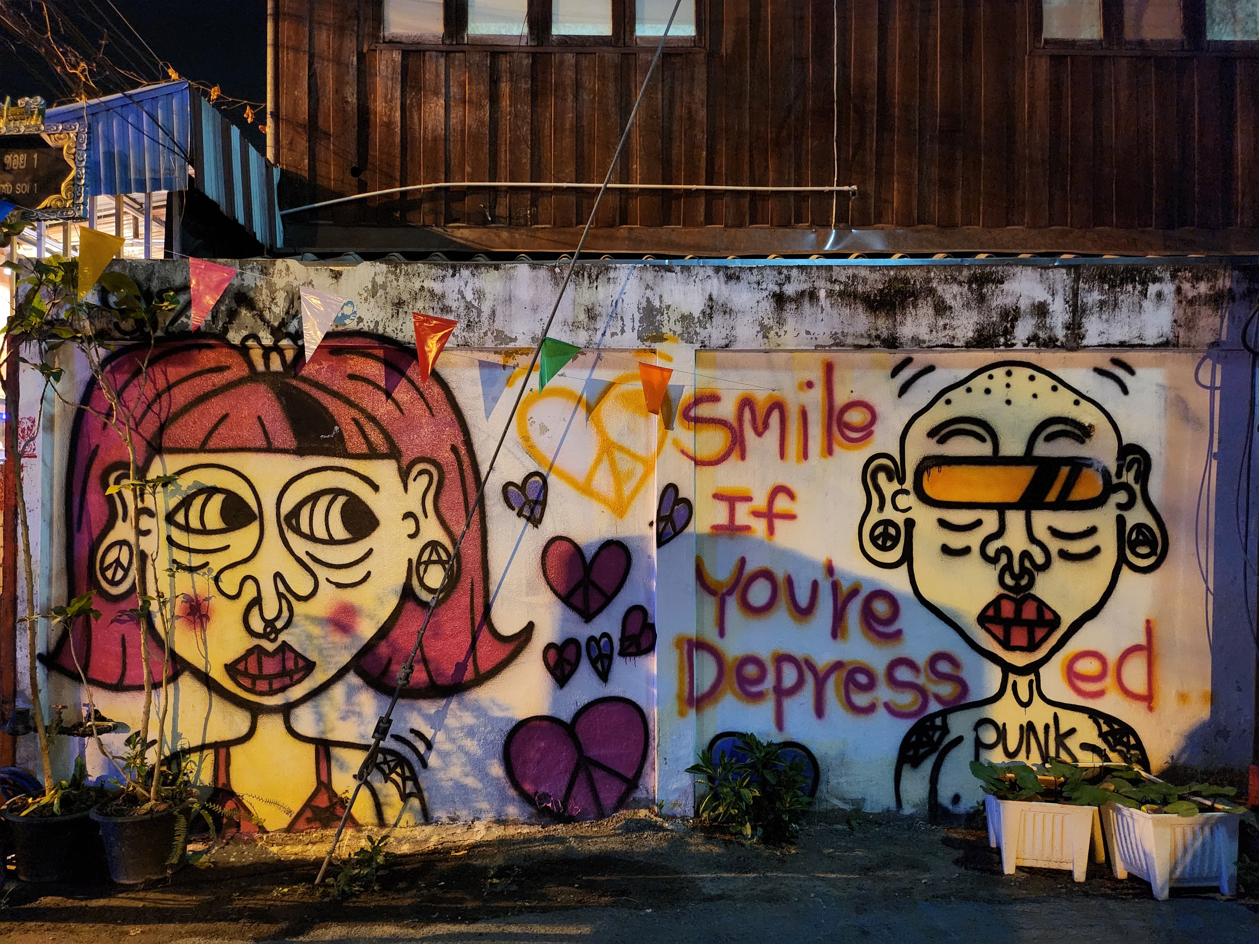 Street art on a wall features two cartoon faces with a peace sign and the text &quot;Smile if you're depressed&quot; and &quot;punk.&quot;