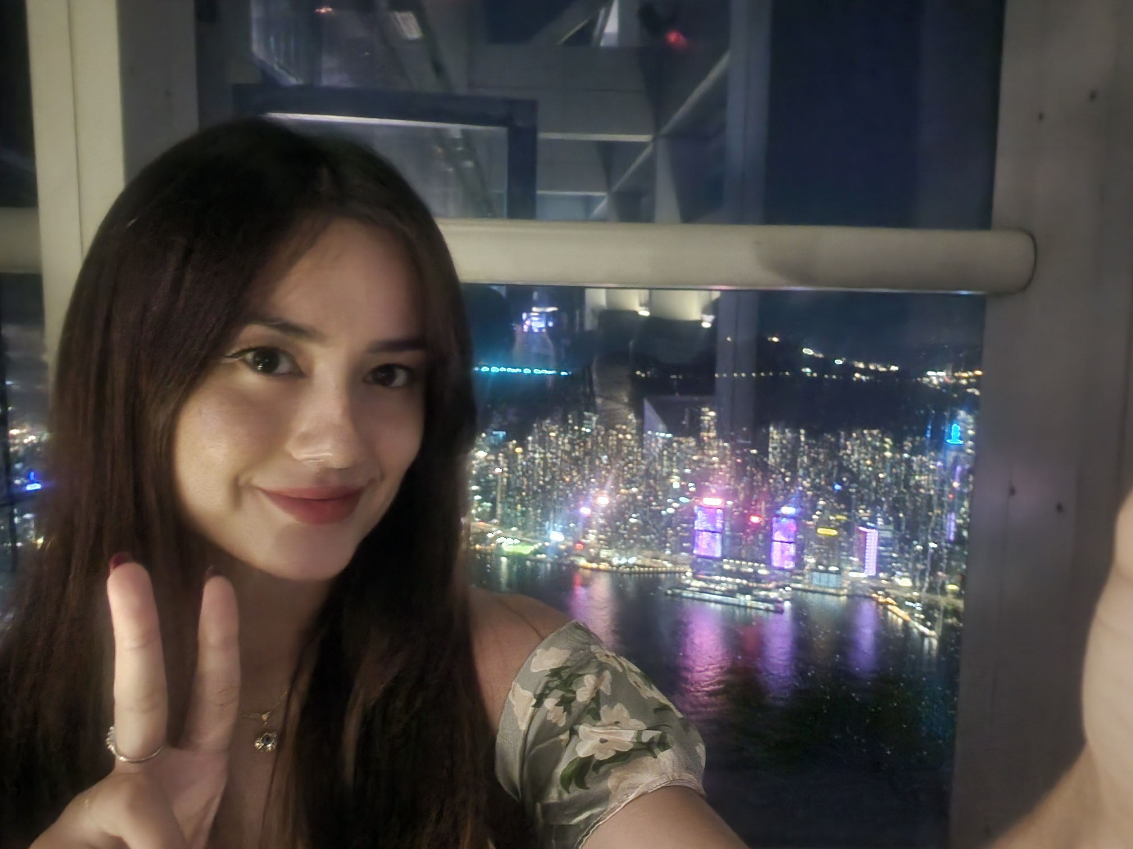The author taking a selfie with a peace sign in front of a cityscape view at night, featuring illuminated skyscrapers