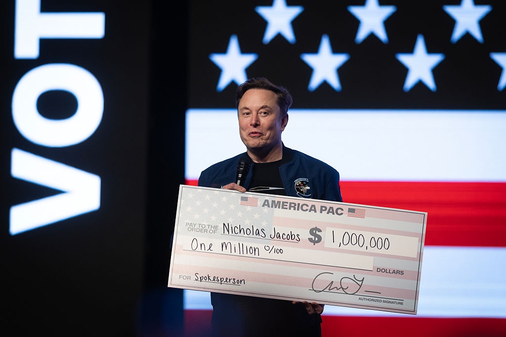 A person holds a large ceremonial check for one million dollars against a backdrop with stars and stripes