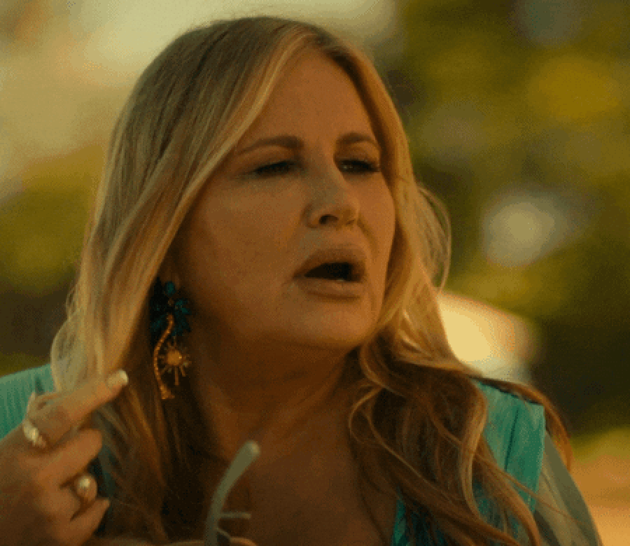 Person outdoors with sunglasses and colorful earrings, holding glasses and looking expressively to the side