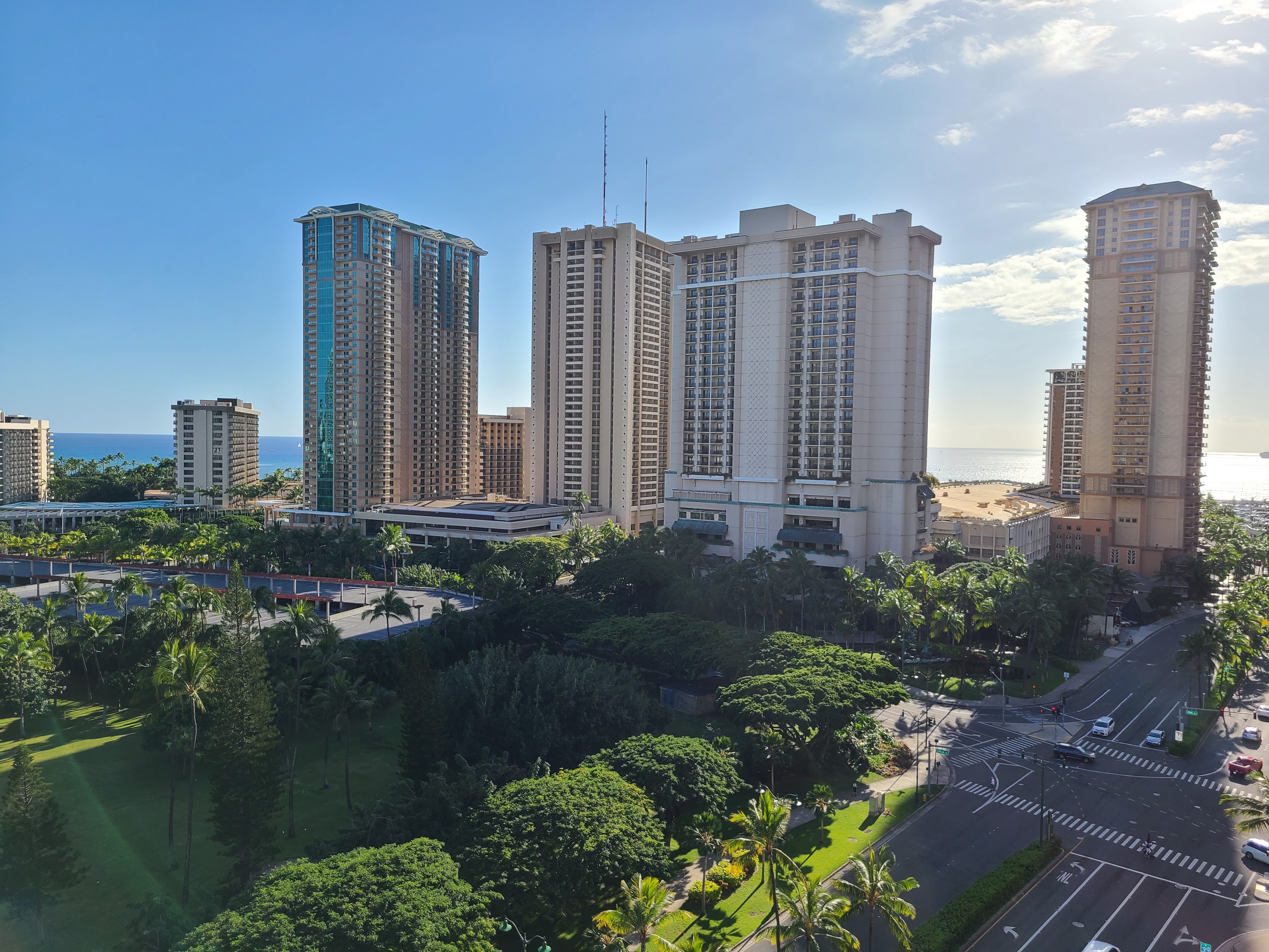 Aerial view of a cityscape featuring tall buildings, lush greenery, and a visible coastline in the distance