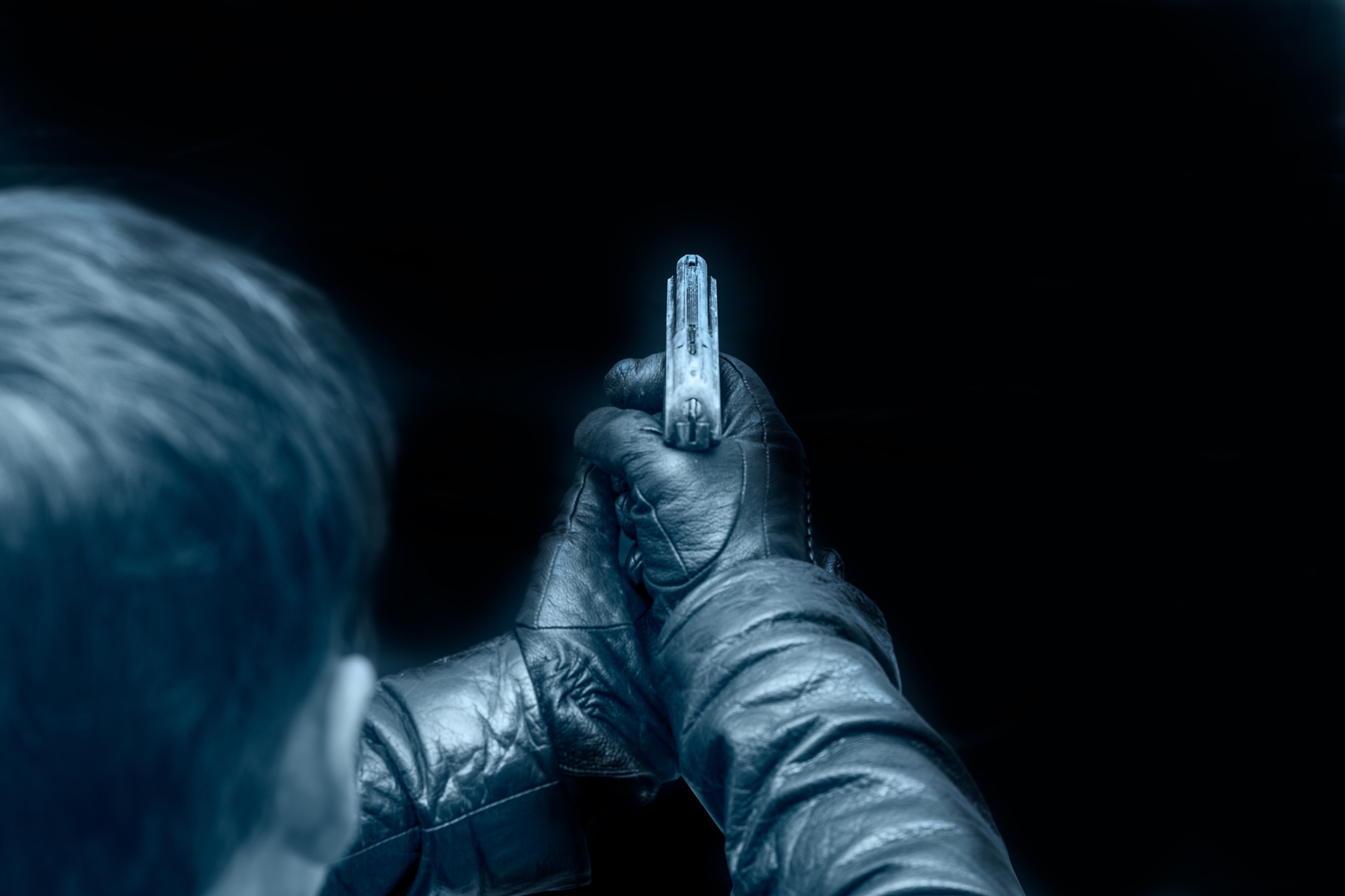 A person wearing gloves holds a gun, aiming it forward in a focused manner, with only their back visible