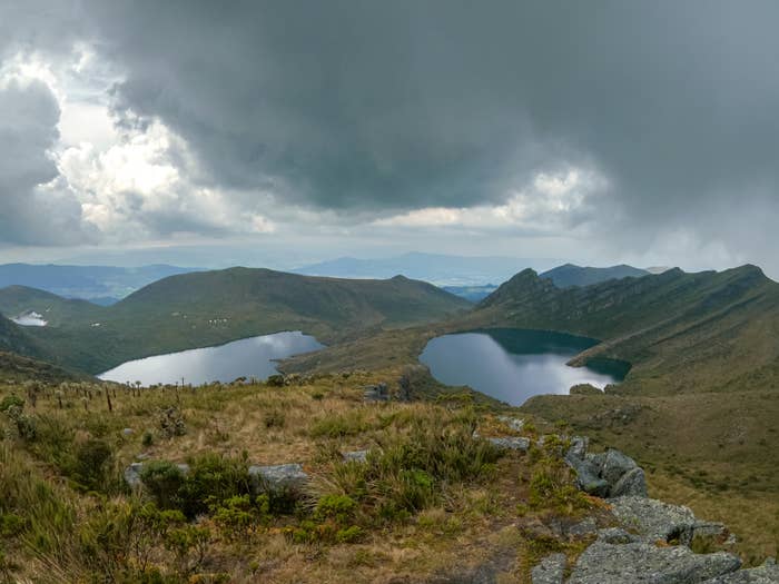 Mountain landscape with two lakes under a cloudy sky, surrounded by grassy terrain and distant hills
