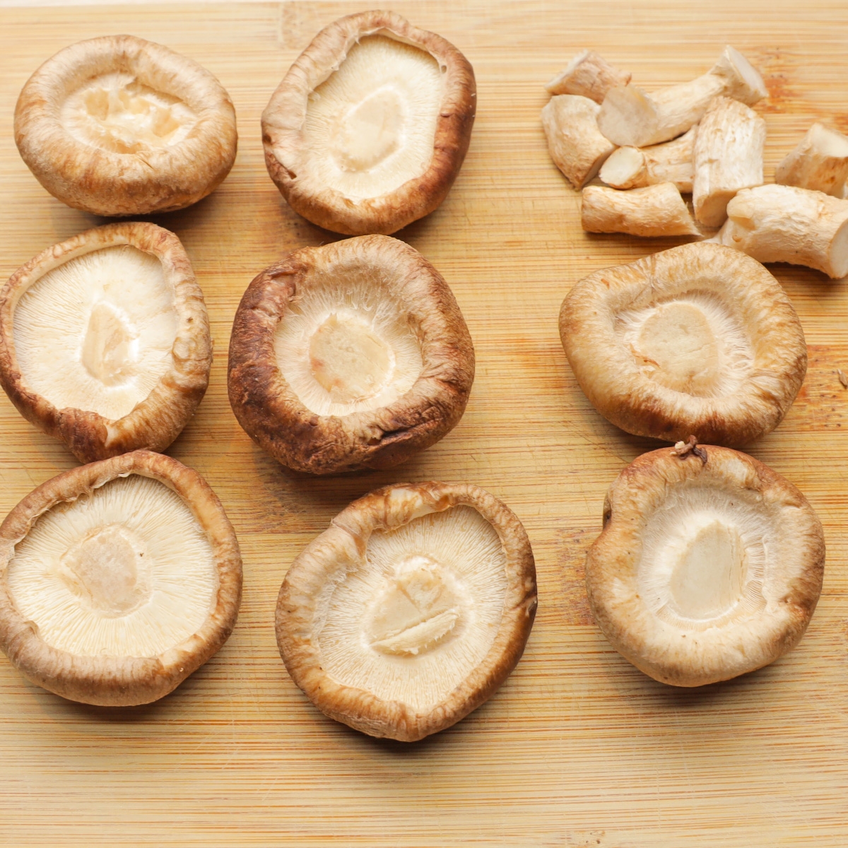 まな板の上に並べられた無造作に切られたシイタケの上面と切られた茎。