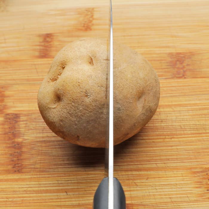 まな板の上で包丁がジャガイモを切ろうとしている様子。