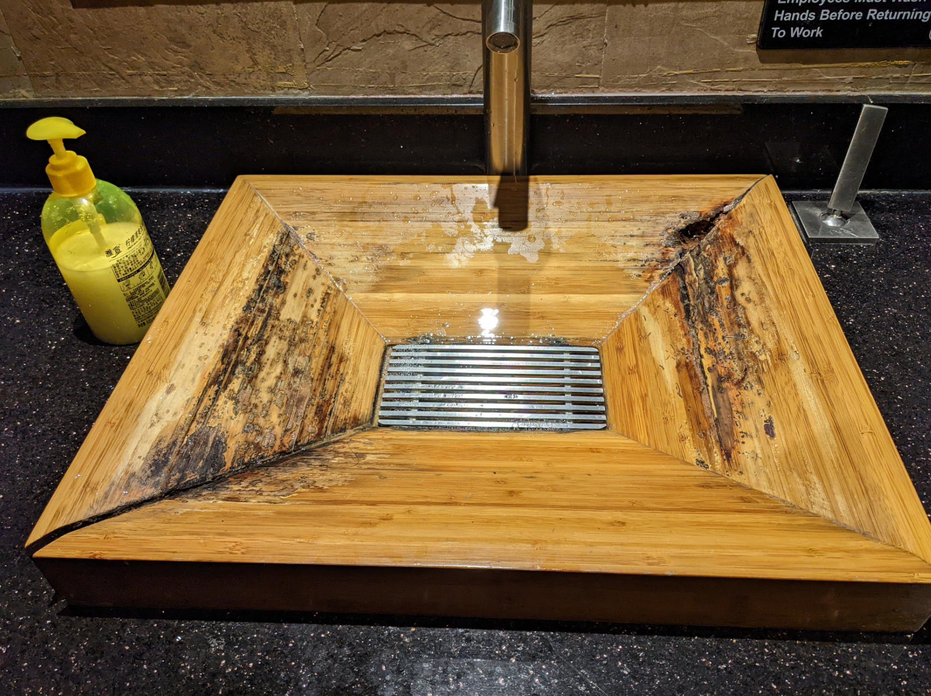 Wooden sink with water damage and mold around the edges. Yellow soap dispenser on the side