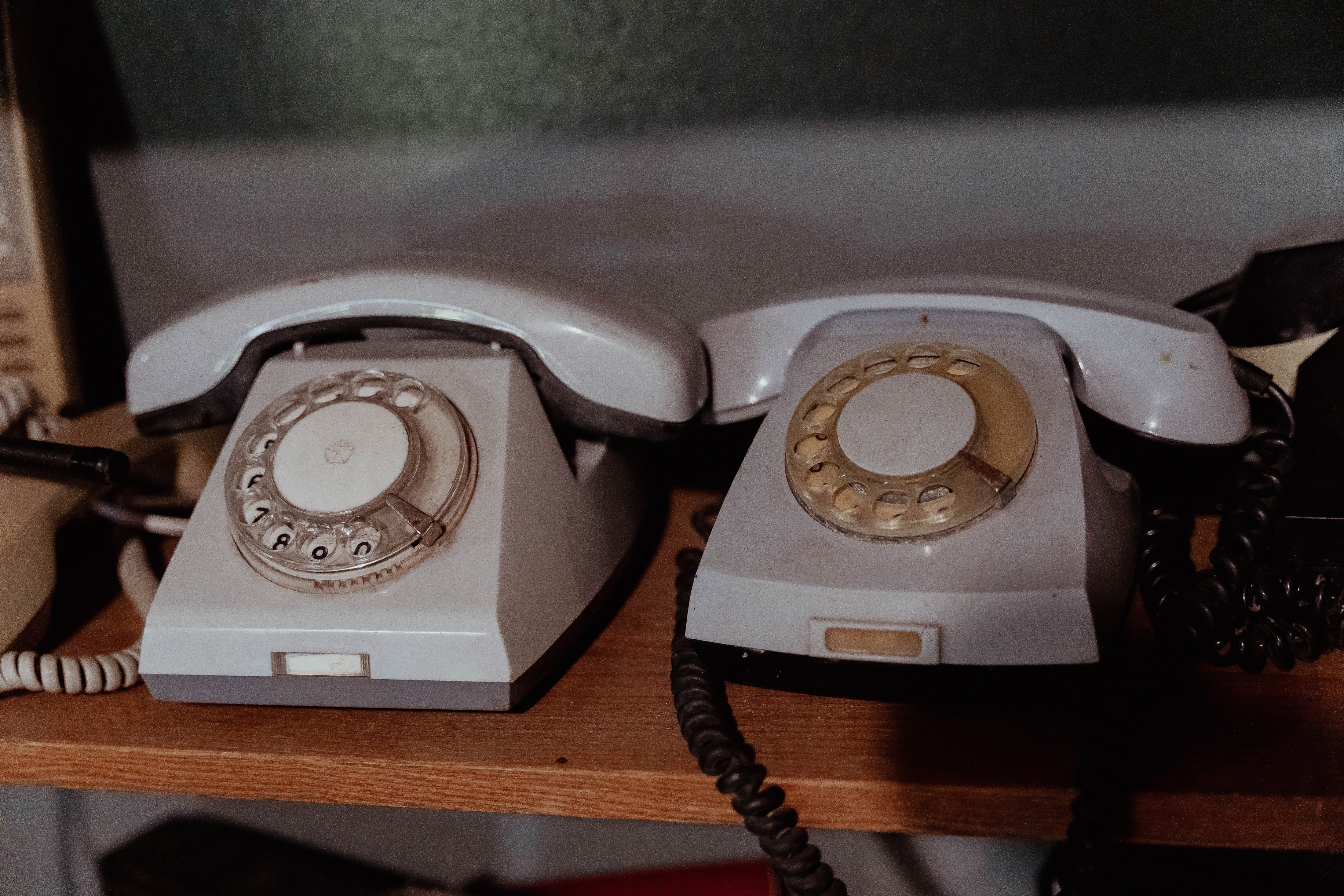 Two vintage rotary phones sit side by side on a wooden shelf, displaying classic mid-20th-century technology