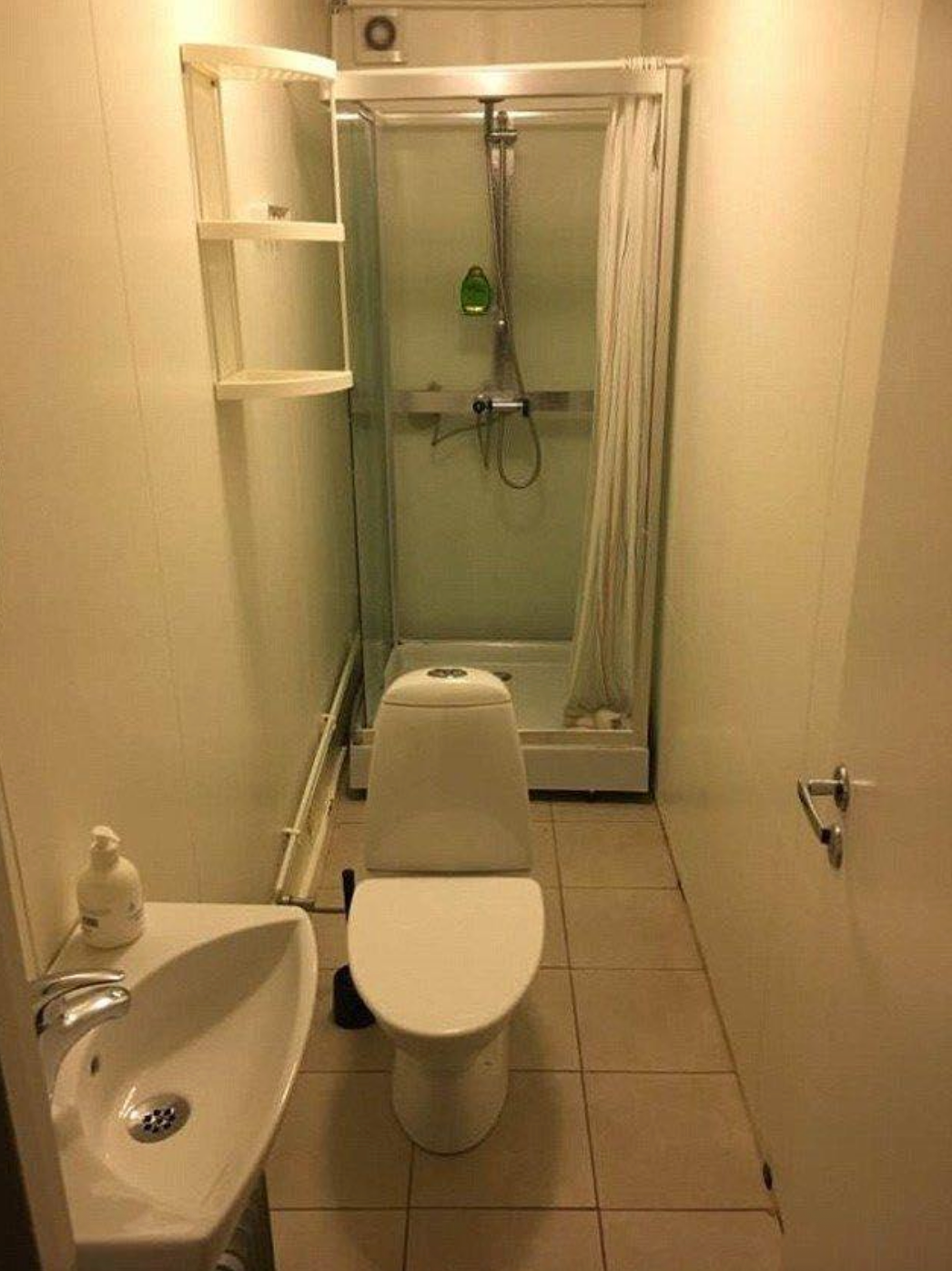 Narrow bathroom with a shower, toilet, and small sink; shower's curtain is partially closed