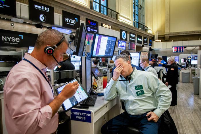Traders work at the New York Stock Exchange; one looks stressed with head in hand, while another observes a tablet screen