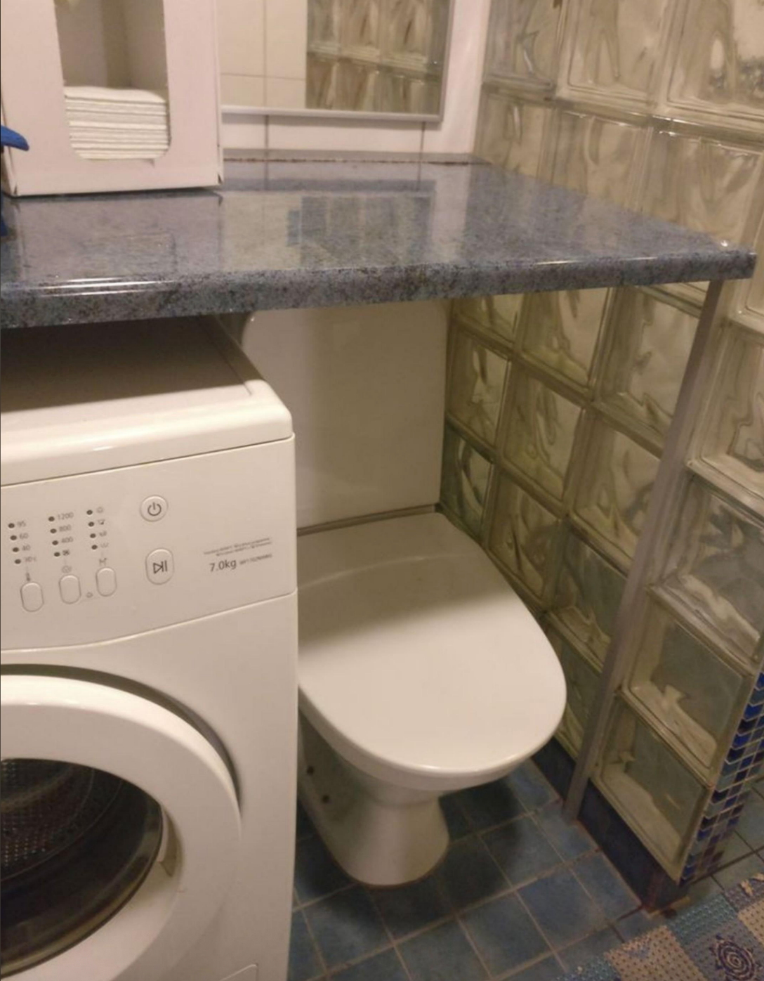 Washing machine and toilet installed closely in a compact space, partially under a countertop
