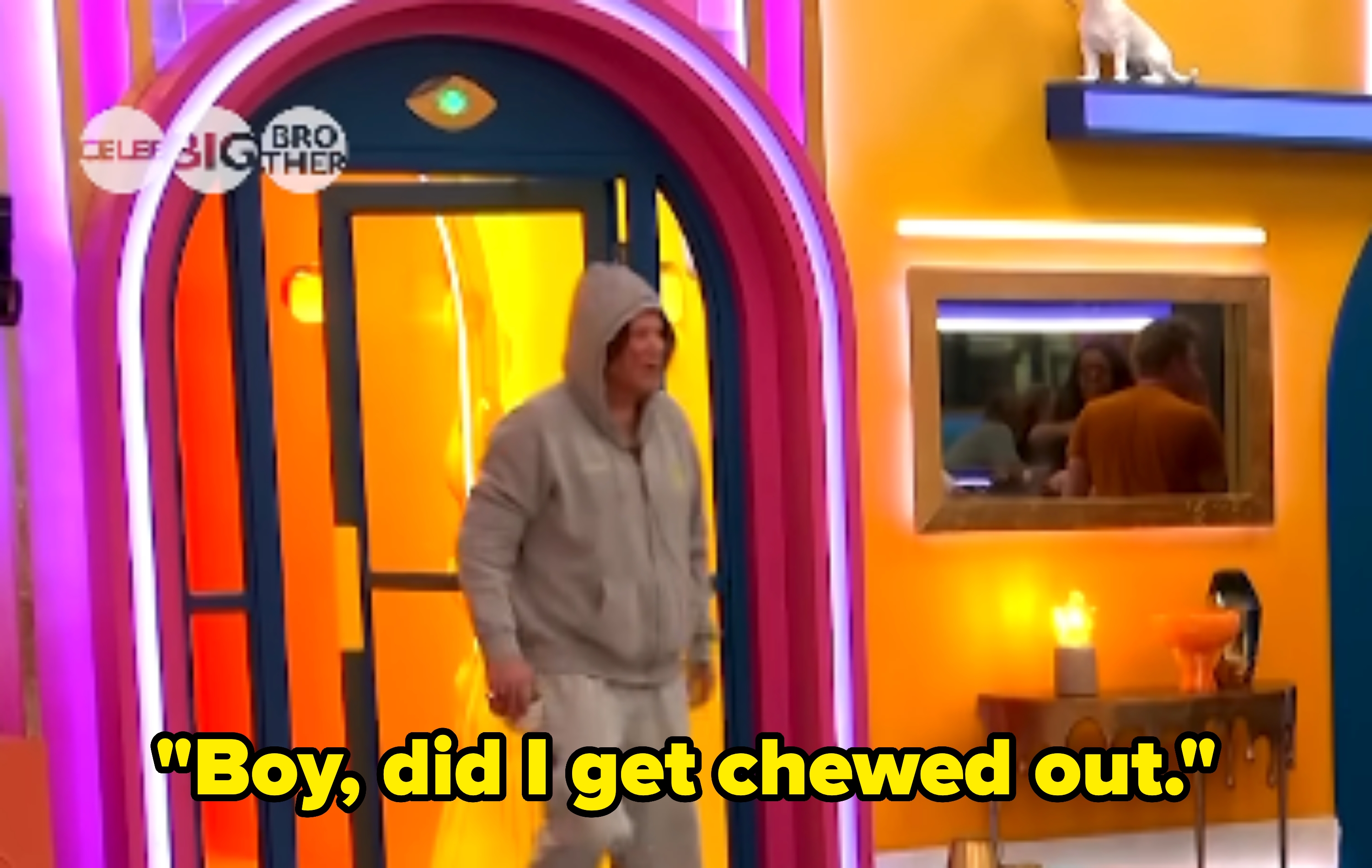 Person in a hoodie and sweatpants entering a brightly lit room in a Big Brother setting