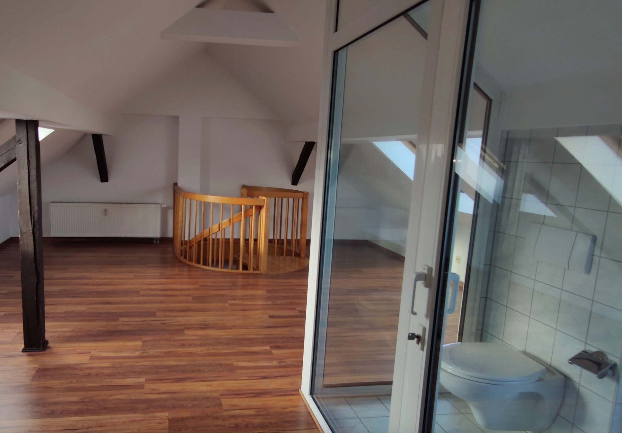 Attic space with wooden floors, a spiral staircase, and a glass-enclosed bathroom area