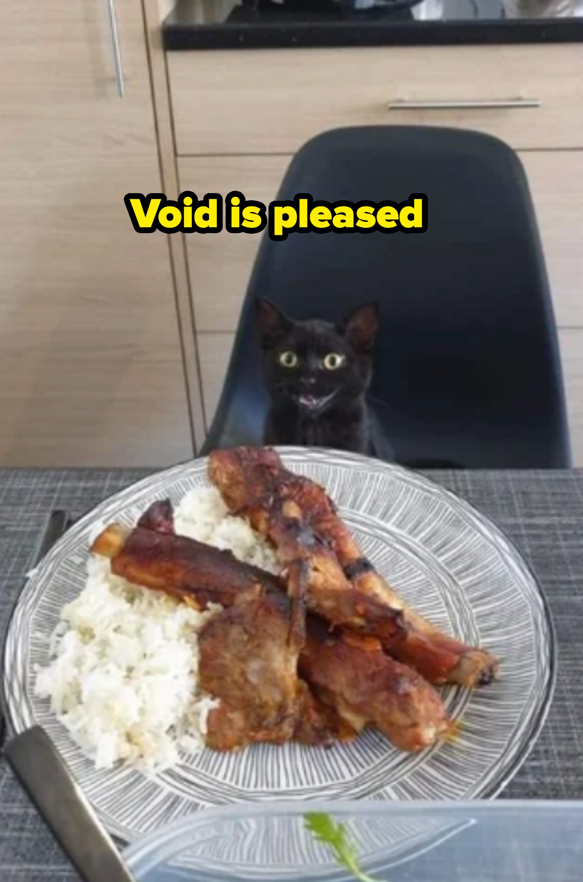 A black cat sits at a table, eagerly eyeing a plate of rice and grilled meats