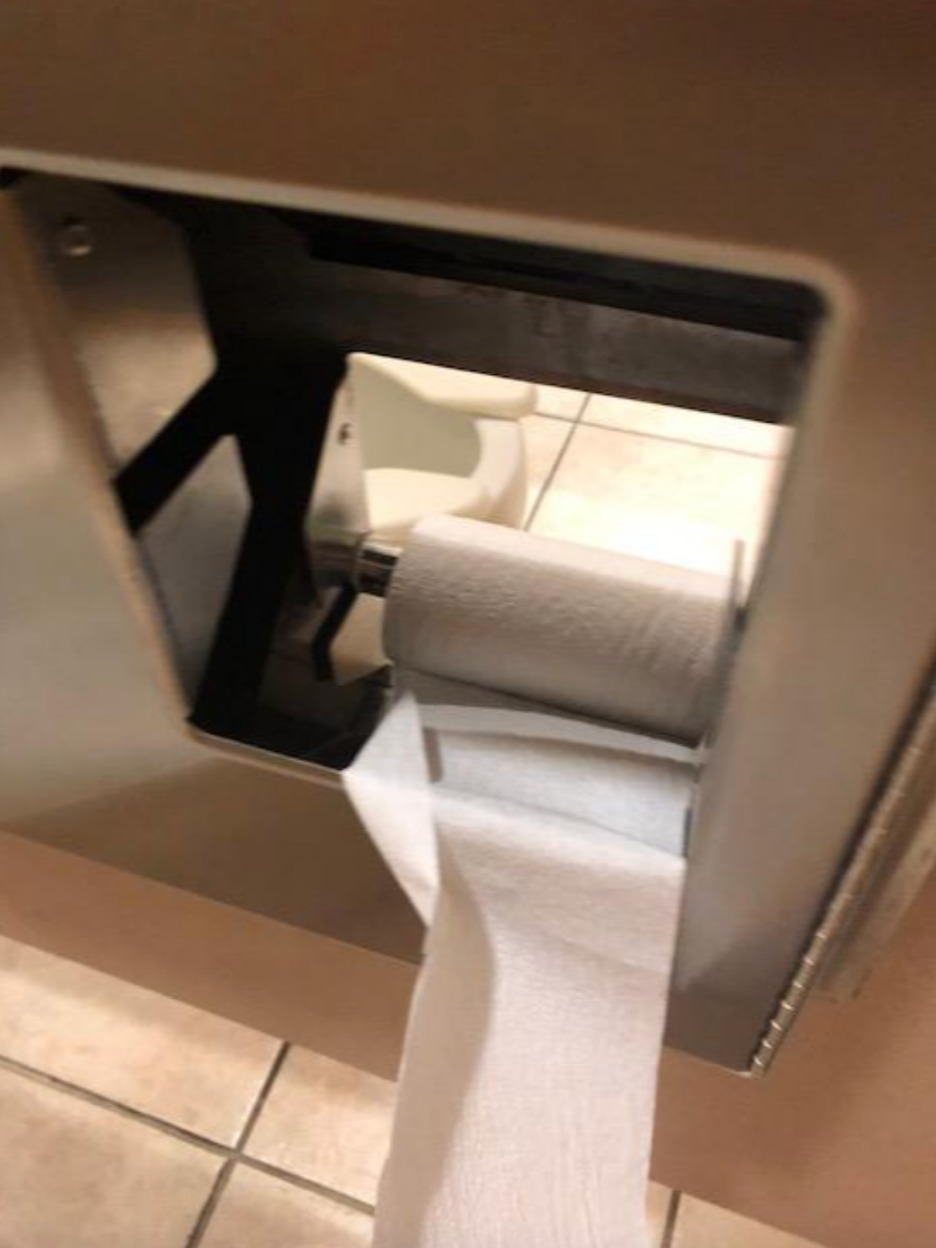 Toilet paper roll mounted in a dispenser, unrolling over the top
