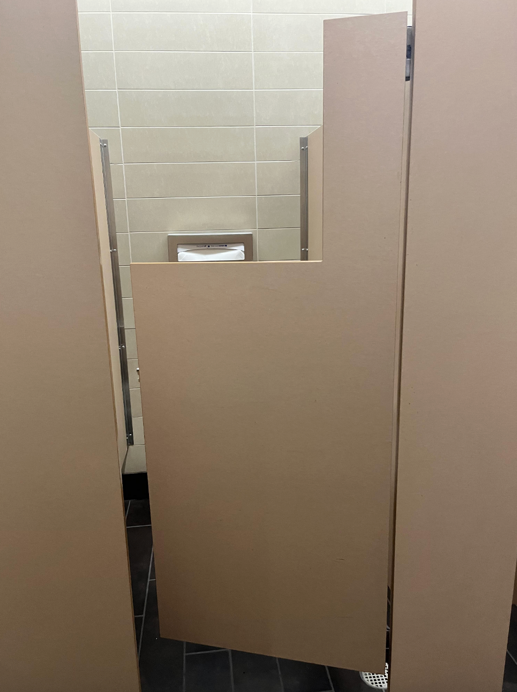 Bathroom stall with a short door, allowing visibility inside, revealing a toilet and paper dispenser