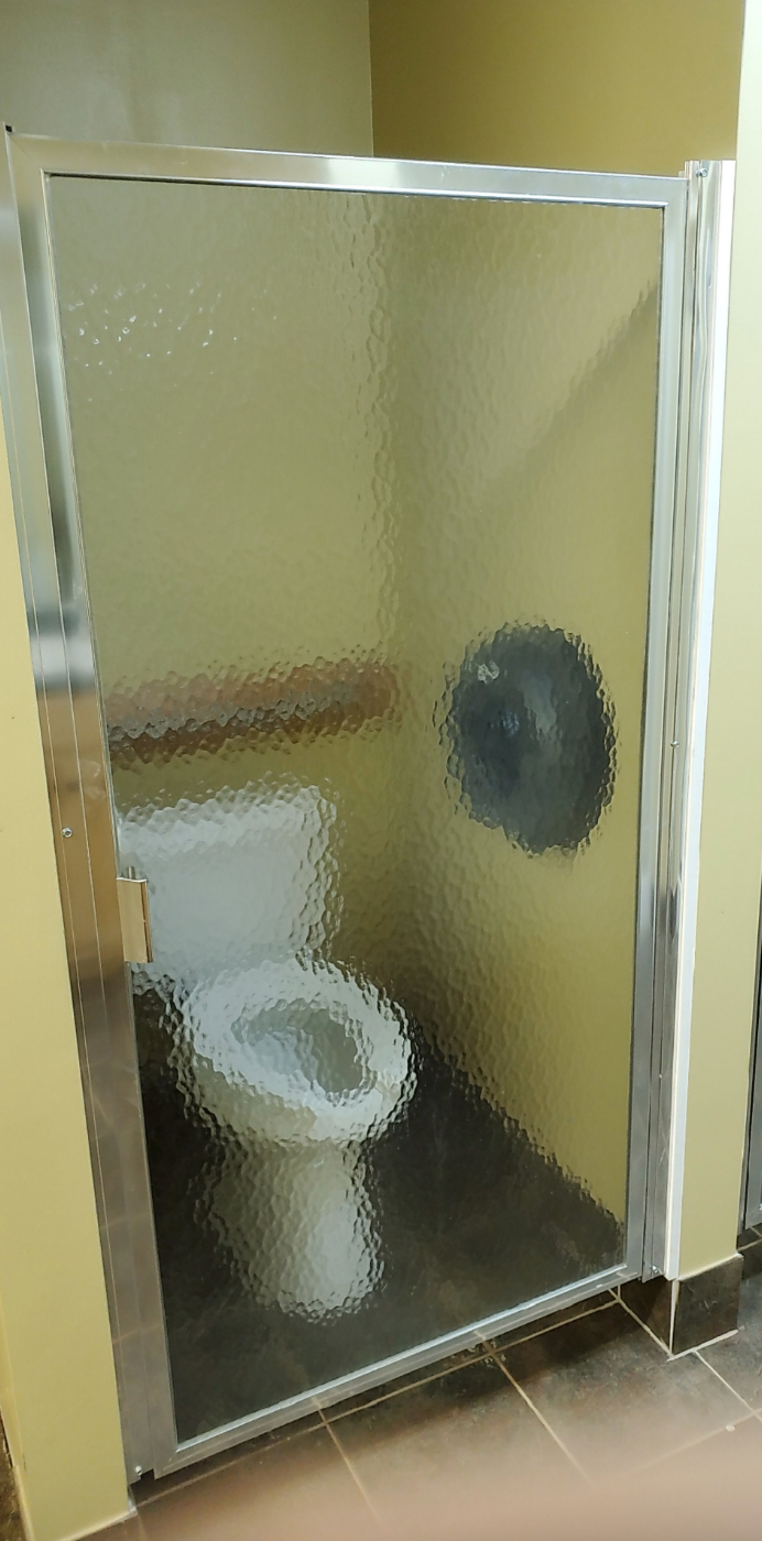 Bathroom stall with a clear, wavy glass door, showing a visible toilet inside