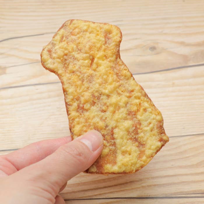 手に持たれた衣のついた揚げ物。板の上に置かれている。