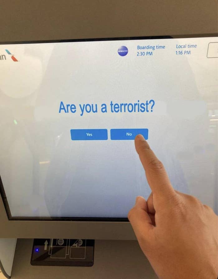 Touchscreen prompt at an airport asks, "Are you a terrorist?" with "Yes" or "No" buttons. A finger points to "No."