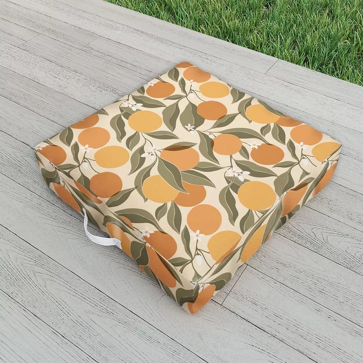 Outdoor seat cushion with a citrus pattern featuring oranges and leaves, placed on a wooden deck near grass