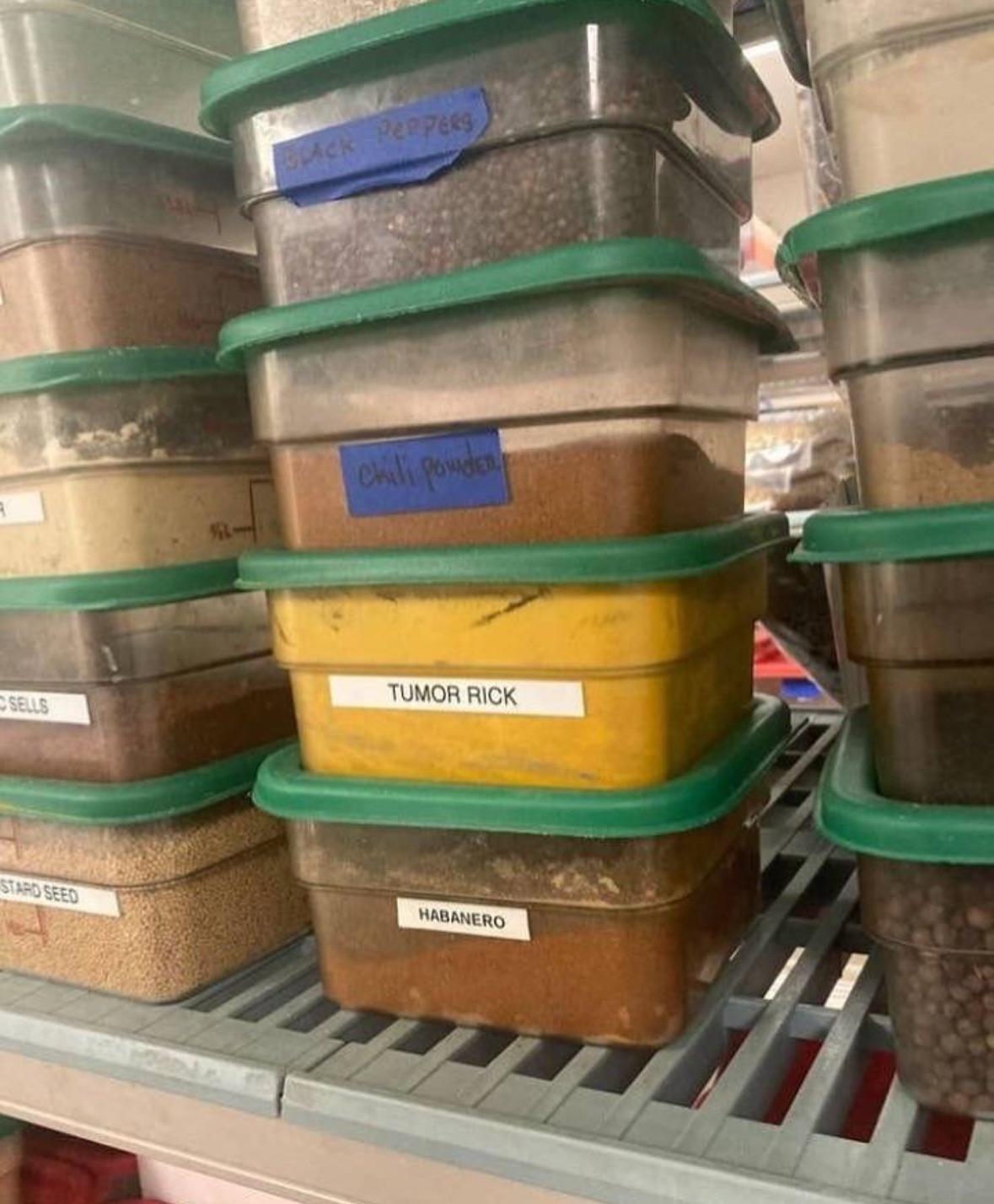 Labeled plastic containers on a shelf, including various spices like "Chili Powder" and "Habanero." One is labeled "Tumor Rick" instead of turmeric