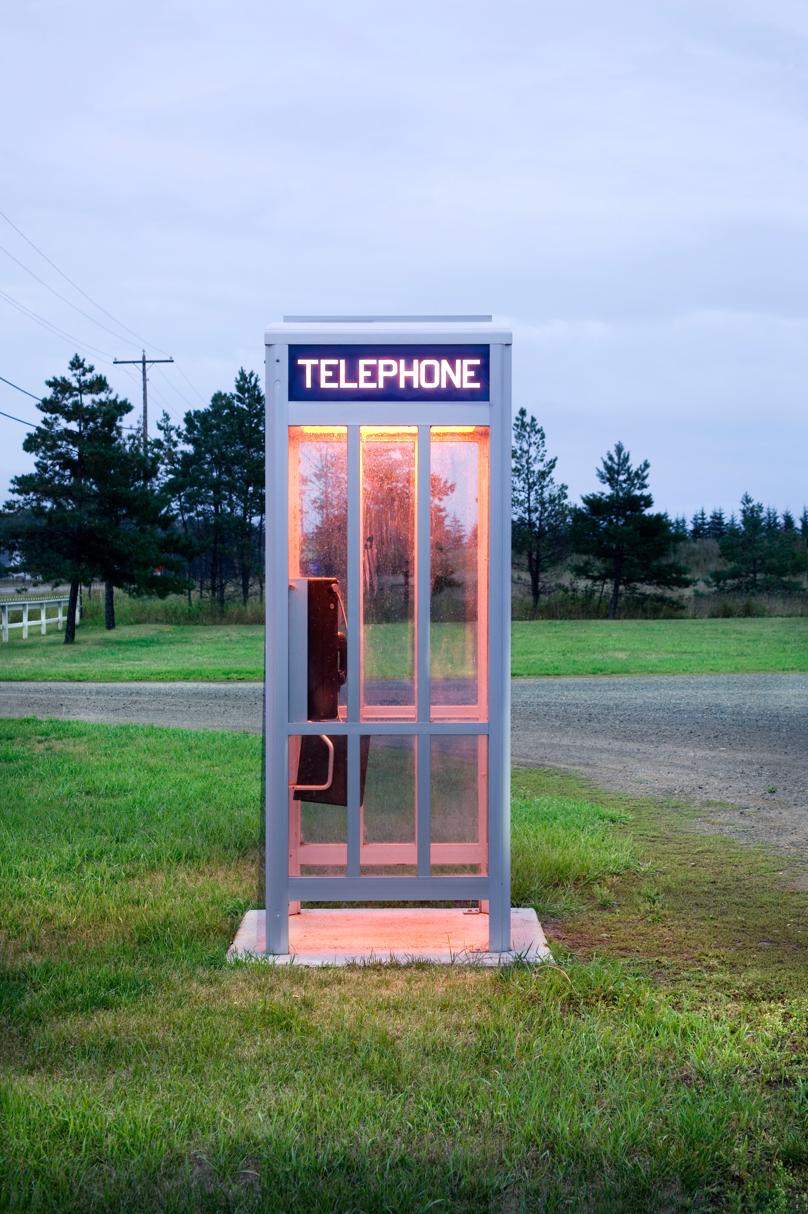 A solitary phone booth stands in an open, grassy field on a cloudy day