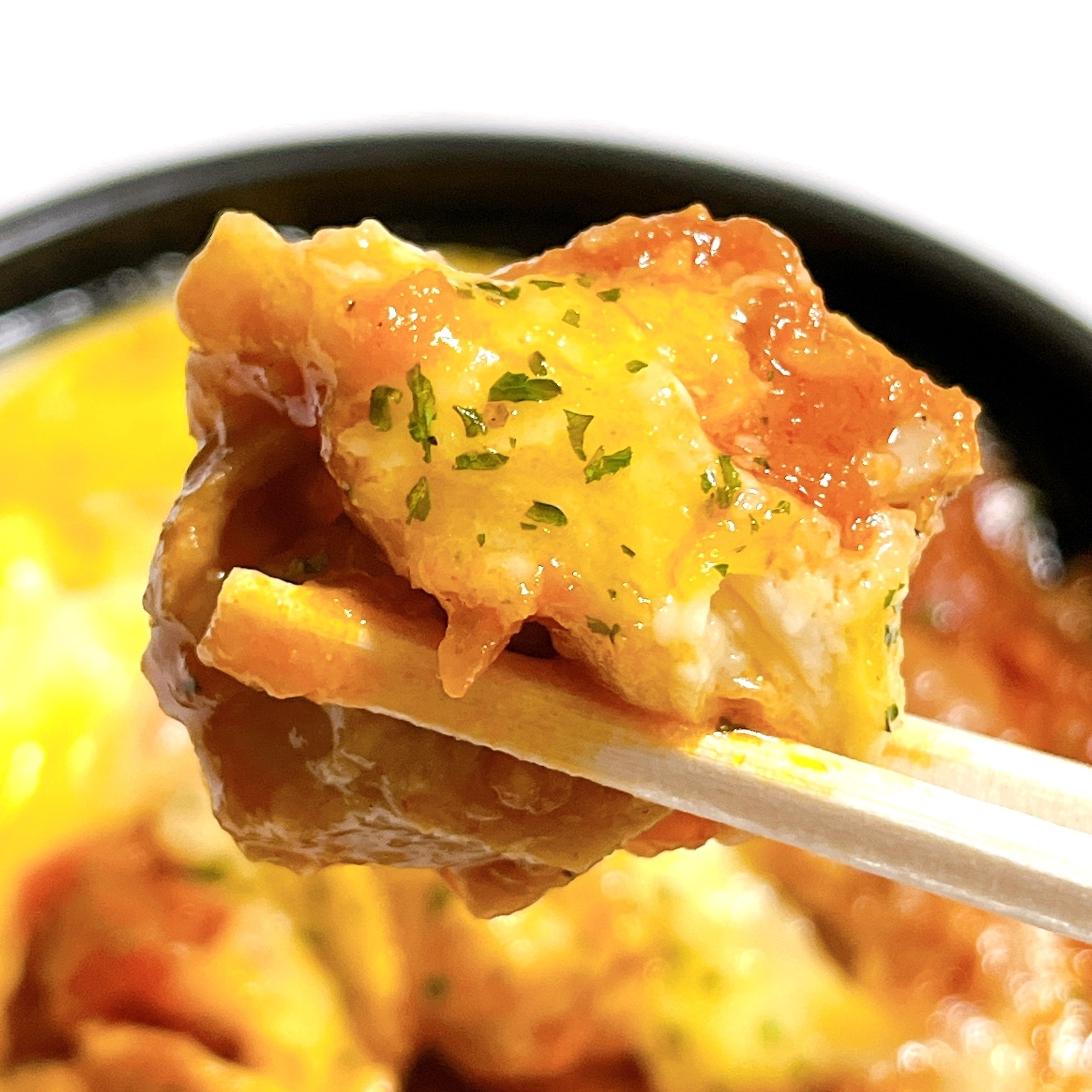 箸で持ち上げられたオムライスのクローズアップ。トマトソースとパセリがかかっています。