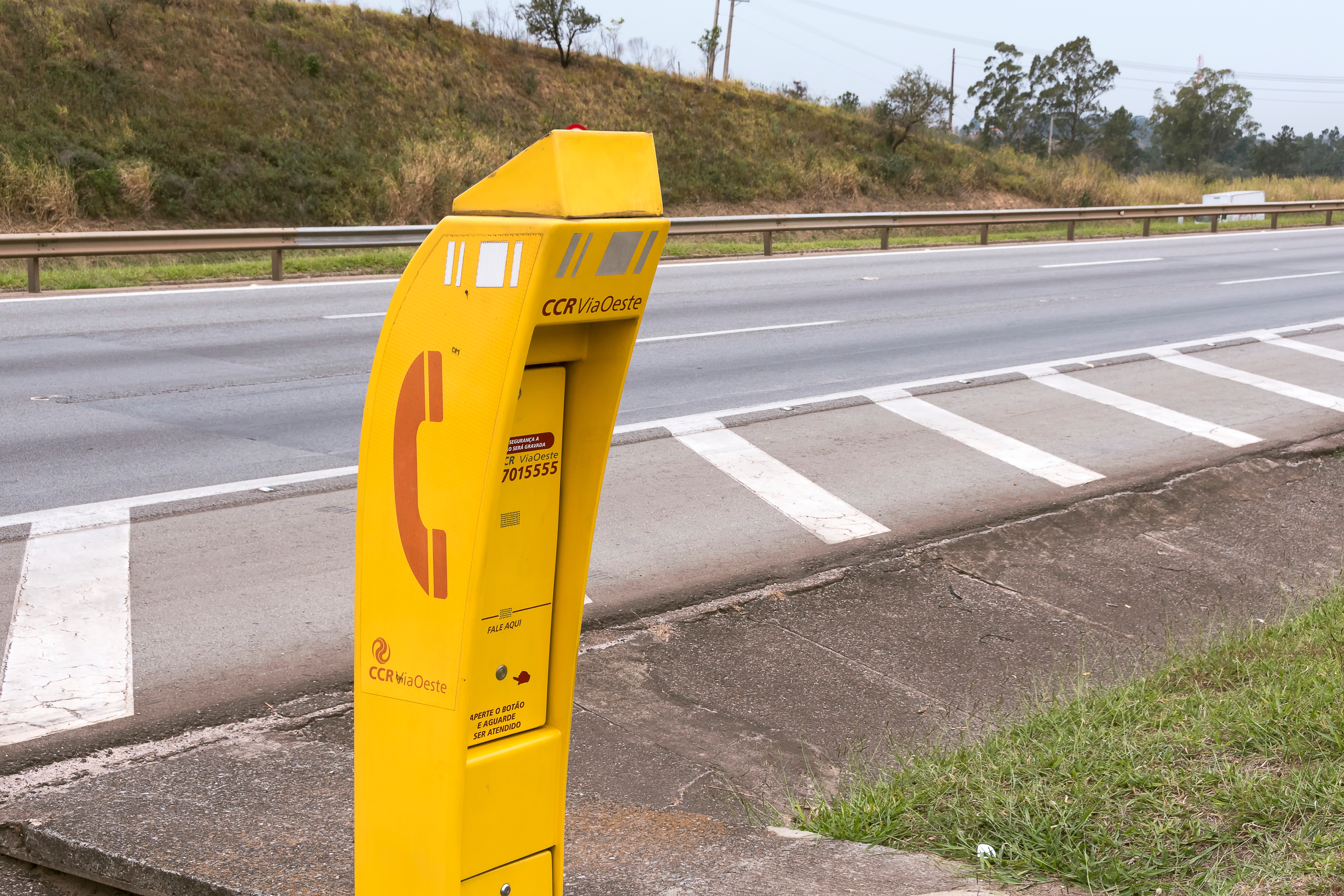 Emergency call box on roadside near highway with striped pavement and grassy area in background