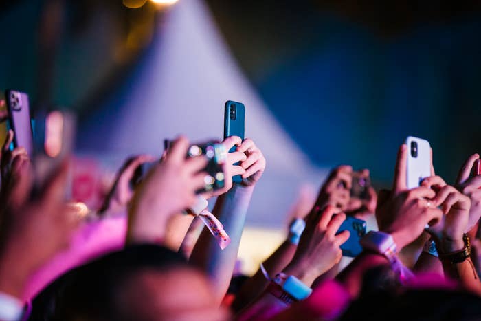 Audience members holding up smartphones, recording an event