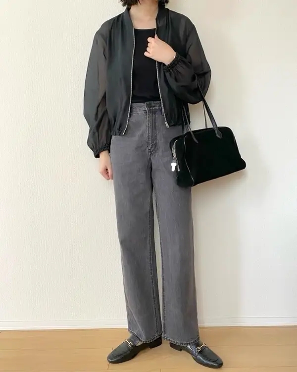 黒のジャケットとシャツ、デニムパンツを着た人物が黒いバッグを持っています。カジュアルなスタイルです。