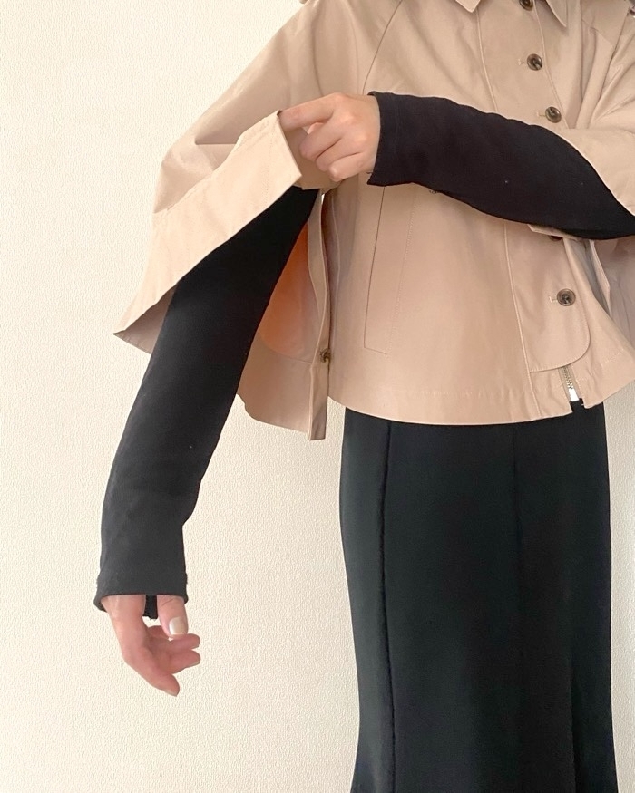 クリーム色のショートジャケットと黒の長袖トップスを着た人がジャケットの袖を調整している。